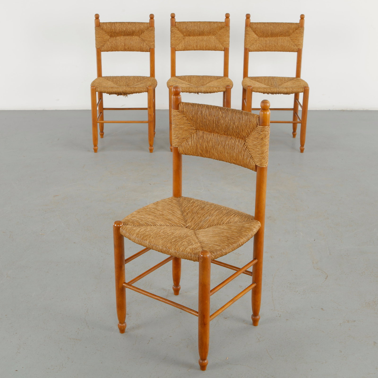 Set of Four Rope and Wood Chairs in the style of Charlotte Perriand, 1960s: A set of four sculptural wooden chairs featuring hand woven rope seats and backs, turned legs, and subtly rounded finials. The warm timber and artisanal construction evoke the rustic modernist vocabul