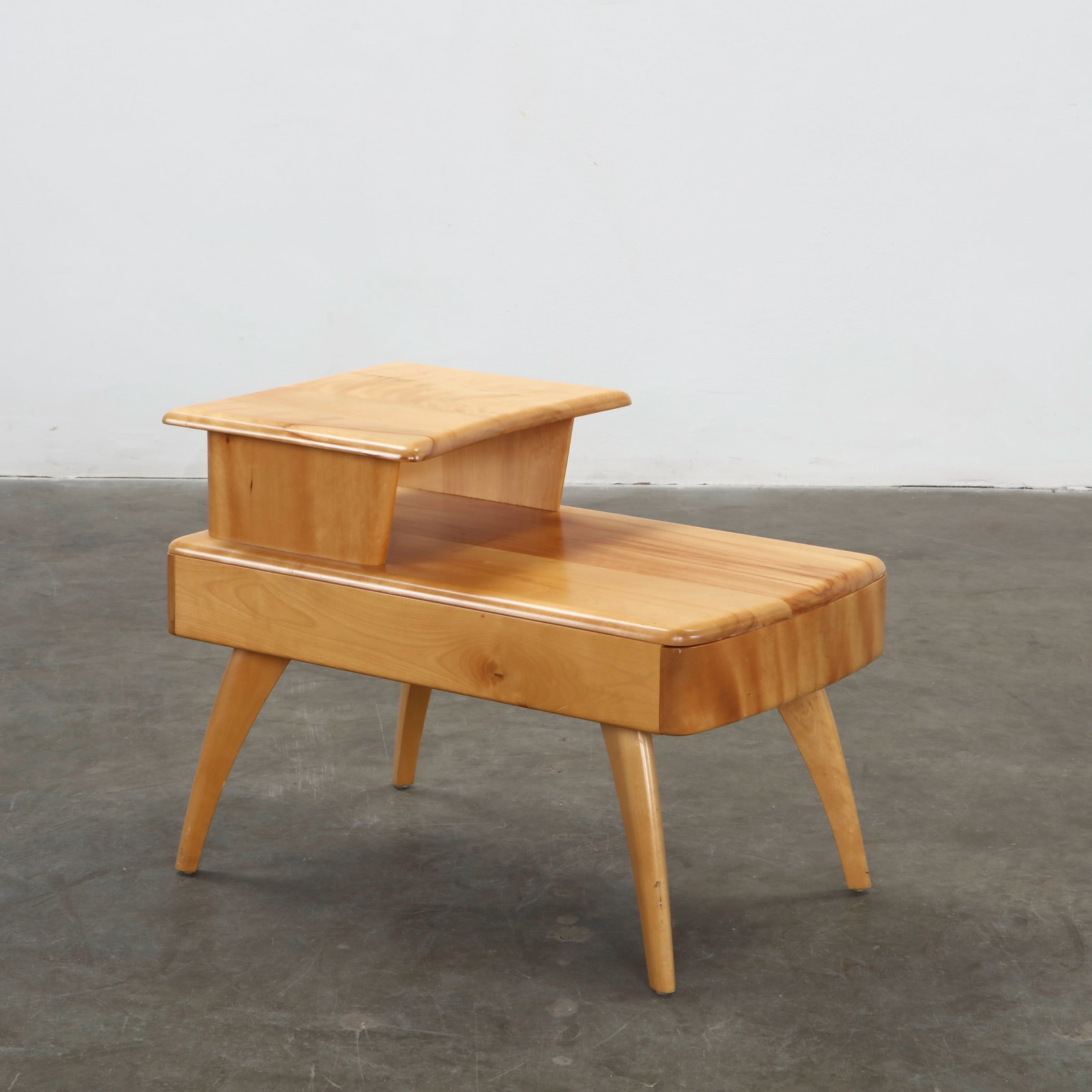 Heywood-Wakefield Mid-Century Modern Step-End Table, 1950s: Executed in solid birch with a warm champagne finish, this sculptural step end table features softly rounded edges and tapered legs characteristic of Heywood Wakefield craftsmanship. The elevated uppe