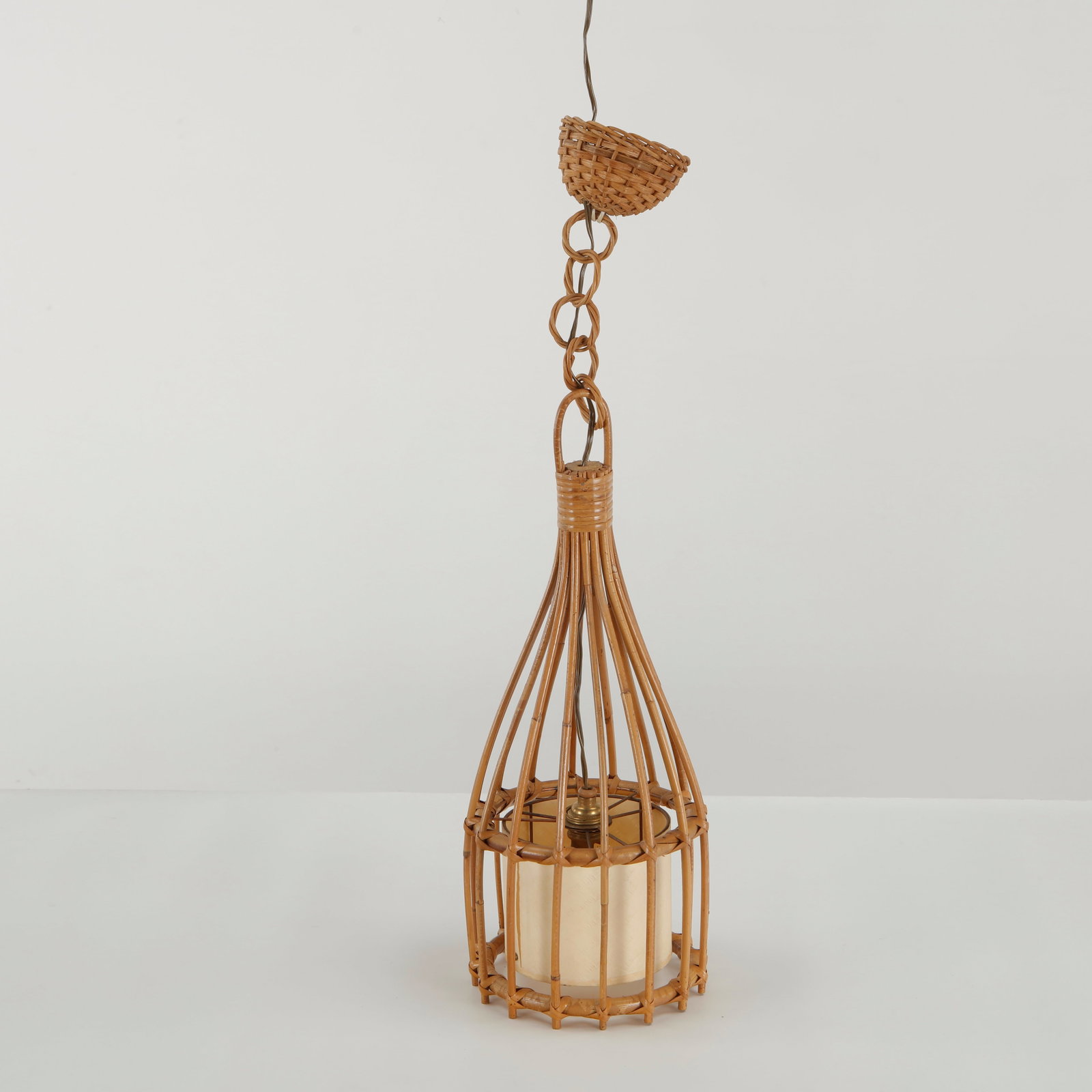 Louis Sognot, Rattan Lantern Pendant Lamp, 1960s: Louis Sognot pendant lamp formed from a delicate rattan framework enclosing a cylindrical textile diffuser. The elongated cage-like construction and suspended rattan chain create a light, atmospheric 