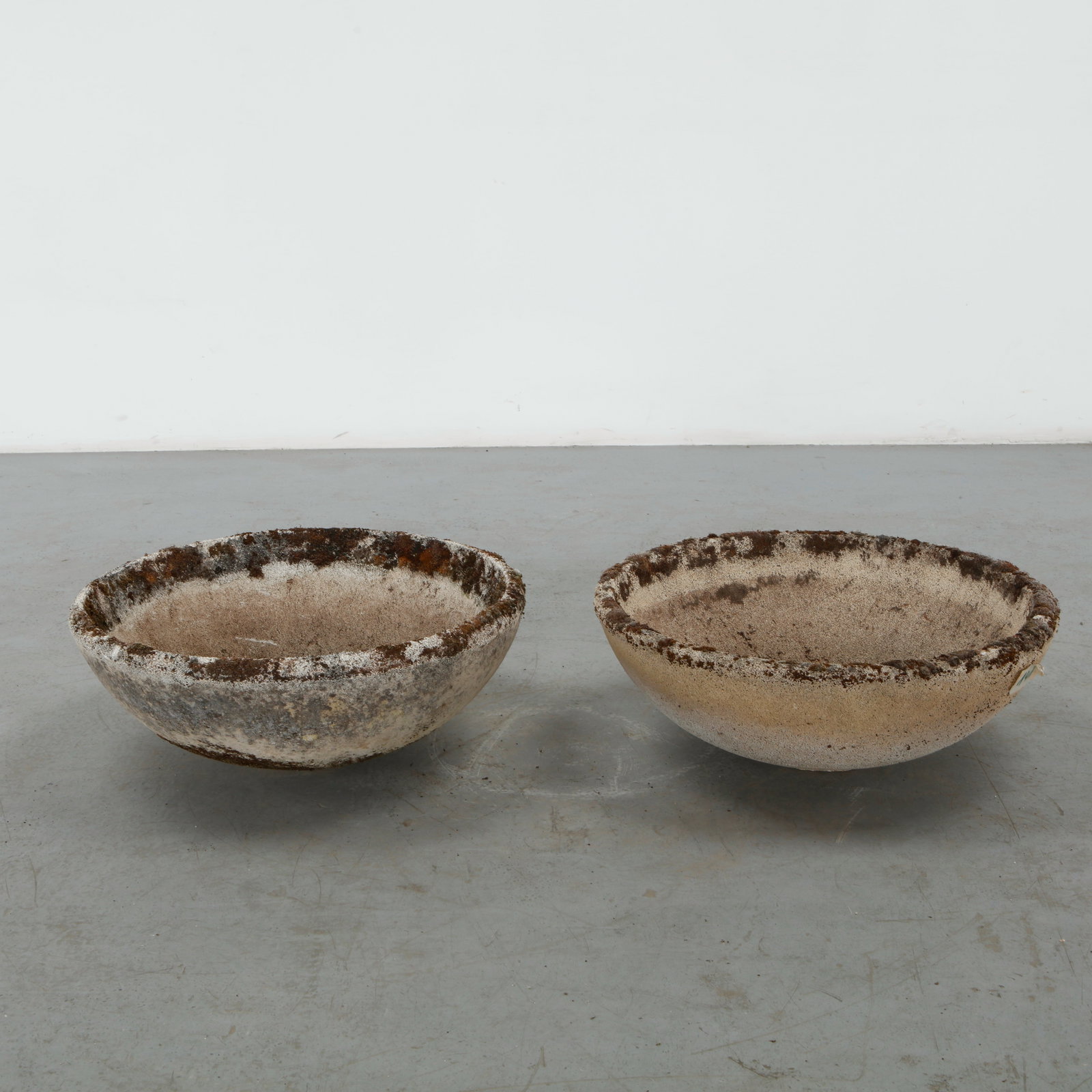 Pair of Cast Stone Bowl Planters, 1960s: A pair of low cast stone bowl planters with wide circular basins and softly rounded profiles. Their varied weathering and mineral patina enhance the tactile quality of the stone and emphasize their ou