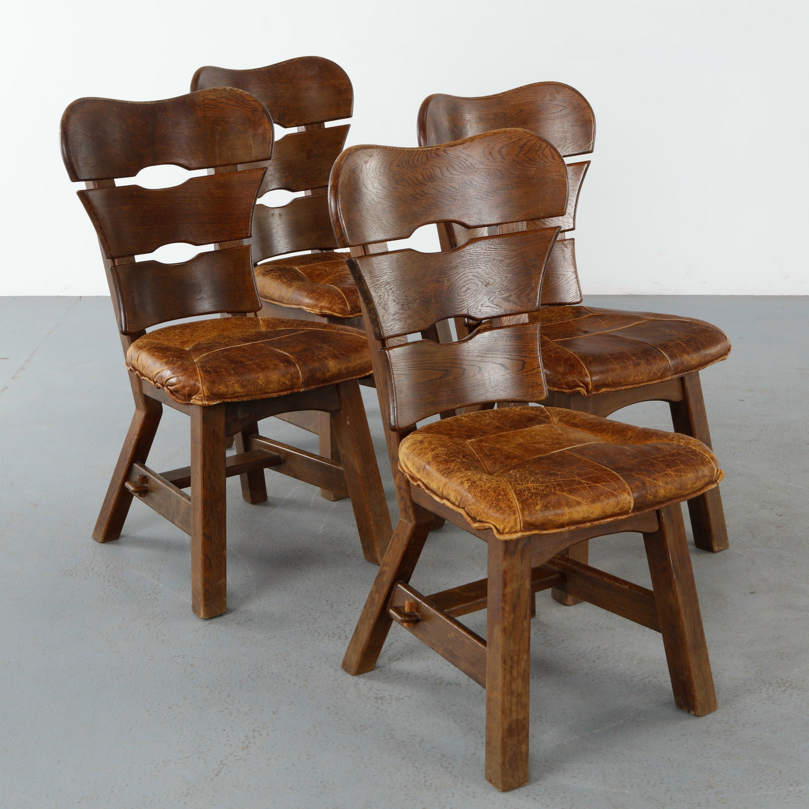 Set of Four French Brutalist Dining Chairs, 1970: Set of four French brutalist dining chairs crafted in solid wood with deeply sculpted ladder backs and richly patinated leather seats. The angular construction and expressive grain exemplify the handc