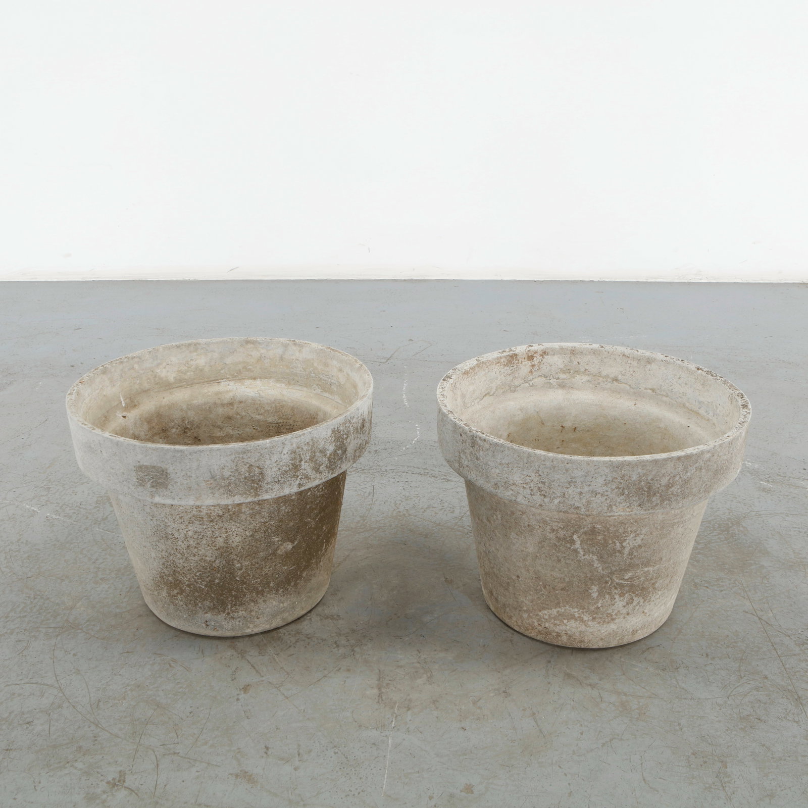 Willy Guhl, Pair of Round Planters, 1960s: Pair of round concrete planters distinguished by their broad cylindrical profiles and substantial rolled rims. Their contrasting weathered surfaces reveal decades of outdoor exposure while retaining t