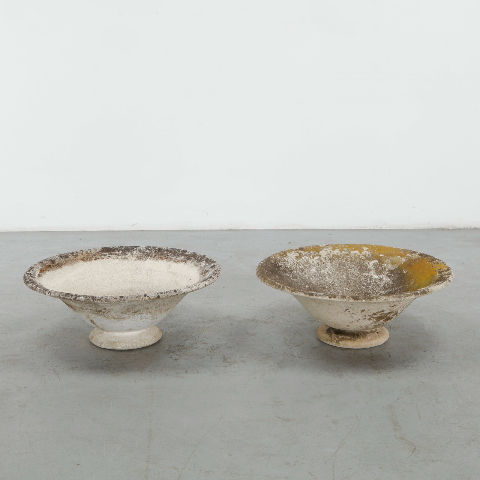 Grandon Fres, Pair of Round Concrete Planters on Stands, 1960s: A rare pair of sculptural concrete planters by Grandon Fres, each formed as a broad, shallow bowl raised on a compact pedestal foot. The weathered surfaces display a richly developed patina of mineral