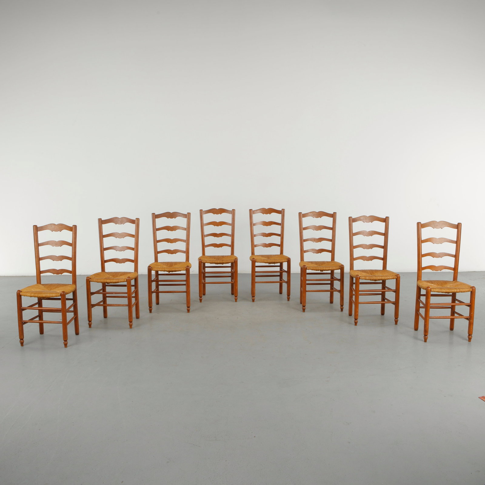 Set of Eight Chairs in the Style of Charlotte Perriand, 1960s: A set of eight wooden dining chairs in the style of Charlotte Perriand, featuring high ladder backs composed of undulating horizontal rails, turned legs and woven rope seats. The expressive repet