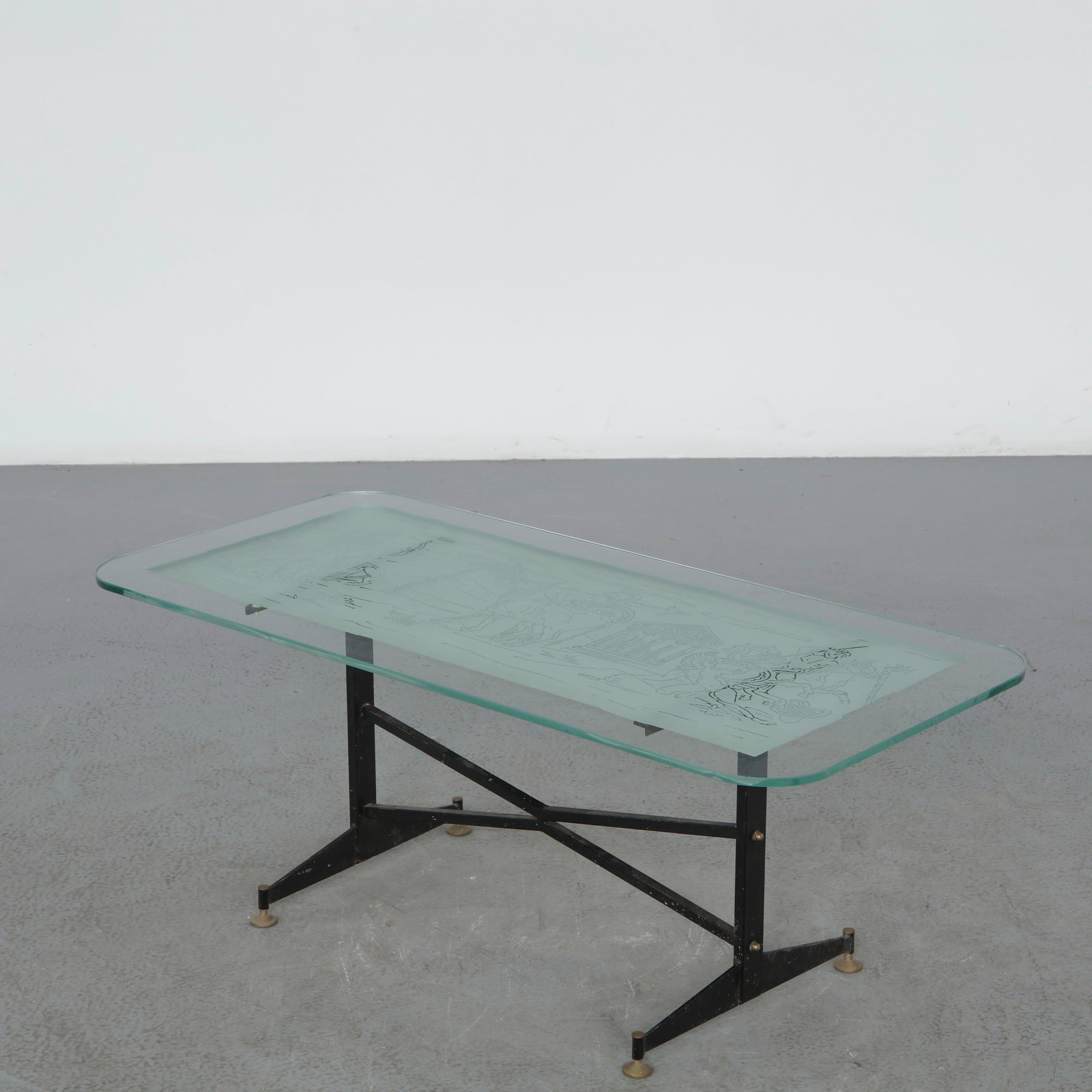 Italian Glass Coffee Table, 1960s: Italian coffee table featuring an etched glass top decorated with classical motifs above a slender black metal frame. The juxtaposition of delicate ornament and minimalist structure reflects the sophi