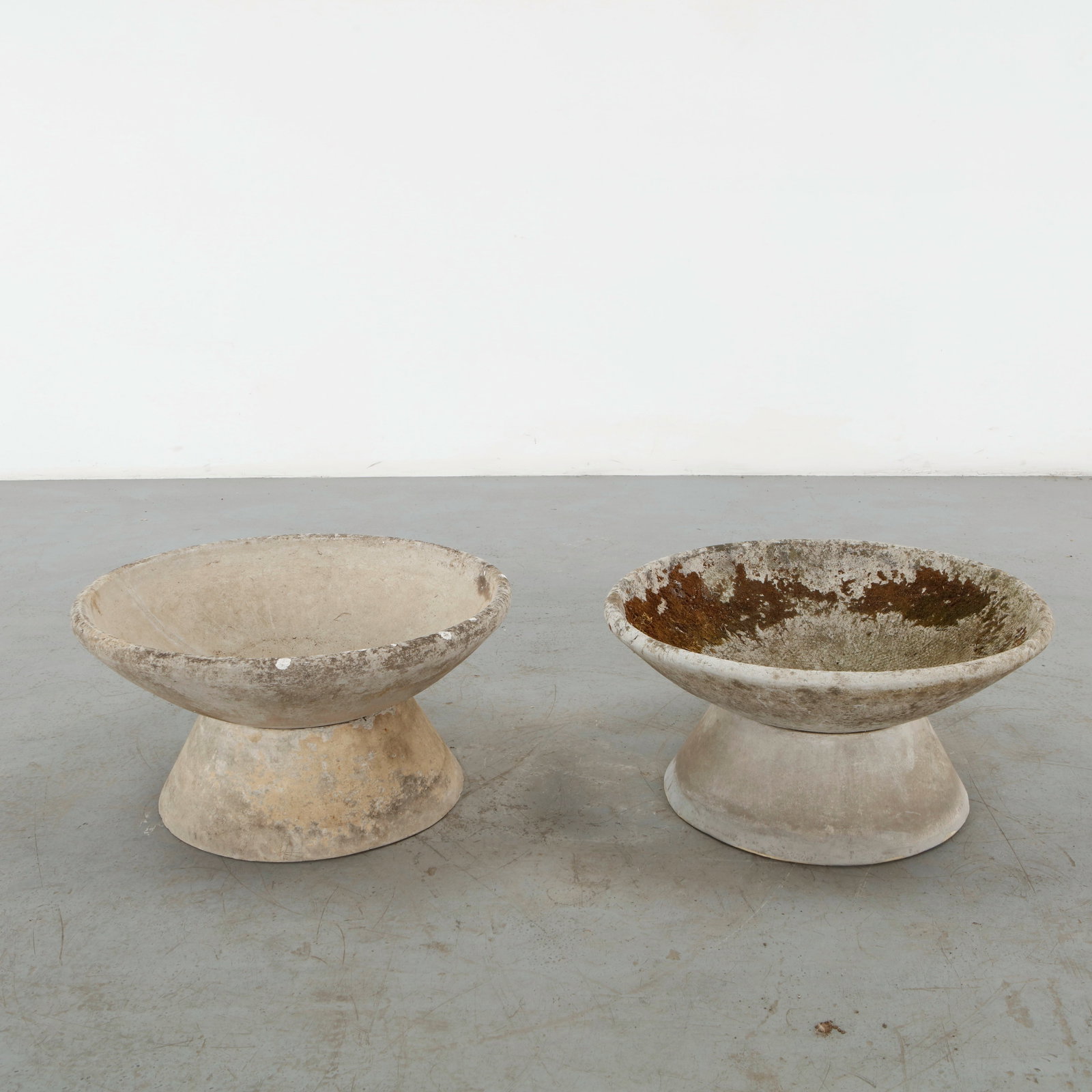 Willy Guhl, Pair of Small Bowl Planters on Concrete Stands, 1960s: A sculptural pair of shallow bowl planters in concrete, each elevated on a broad, tapered pedestal. Their restrained modernist geometry and naturally weathered mineral patina exemplify Guhl enduring a