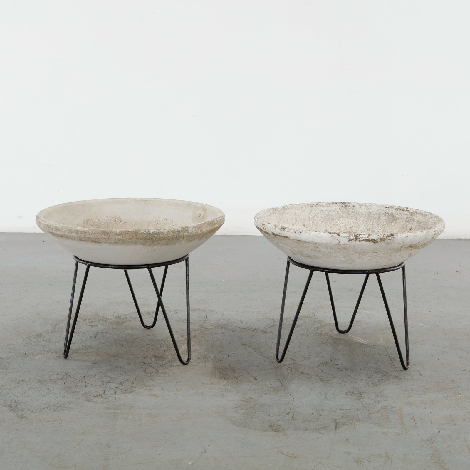 Willy Guhl, Pair of Small Bowl Planters on Stands, 1960s: A pair of shallow concrete bowl planters raised on slender black metal stands, creating a striking contrast between substantial mineral forms and delicate geometric supports. The weathered surfaces
