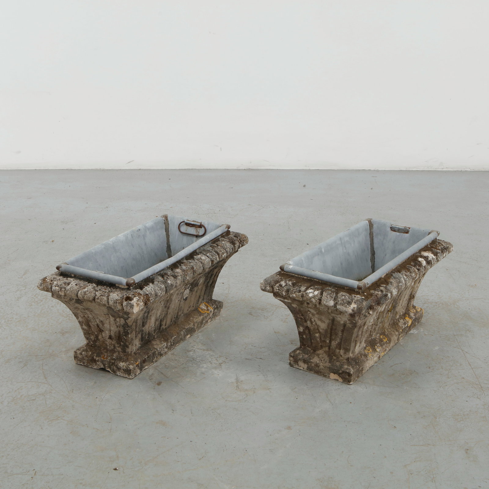 Pair of Rectangular Concrete Planters, 1960s: A pair of robust concrete planters featuring architectural rectangular bodies with pronounced ornamental rims and stepped bases. Their heavily weathered surfaces lend the forms an expressive patina,