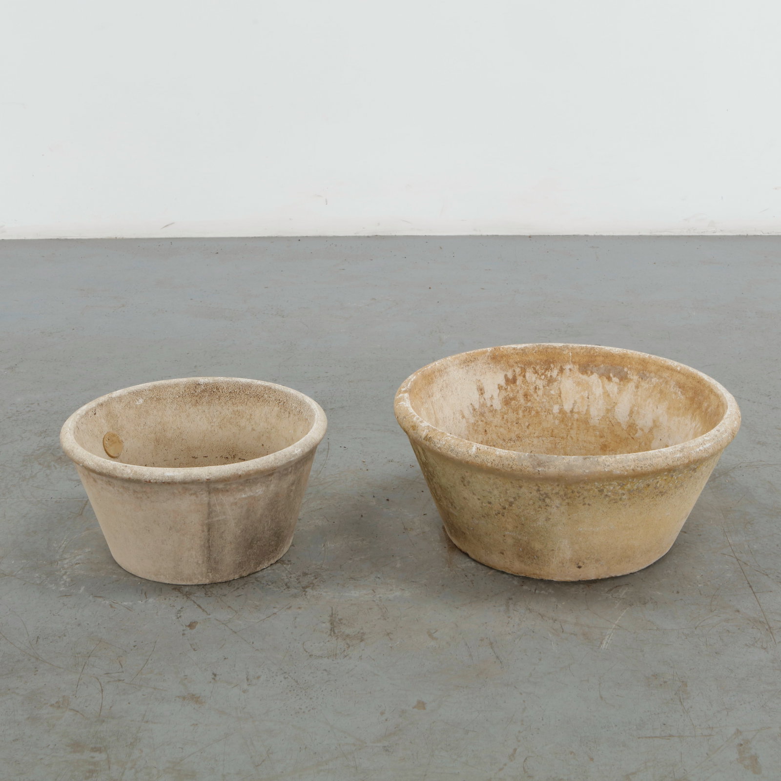 Grandon Fres, Pair of Round Planters, 1960s: A pair of round cast concrete planters in complementary sizes, each formed with a broad circular rim and gently tapered body. Their richly weathered surfaces and natural tonal variation emphasize thei