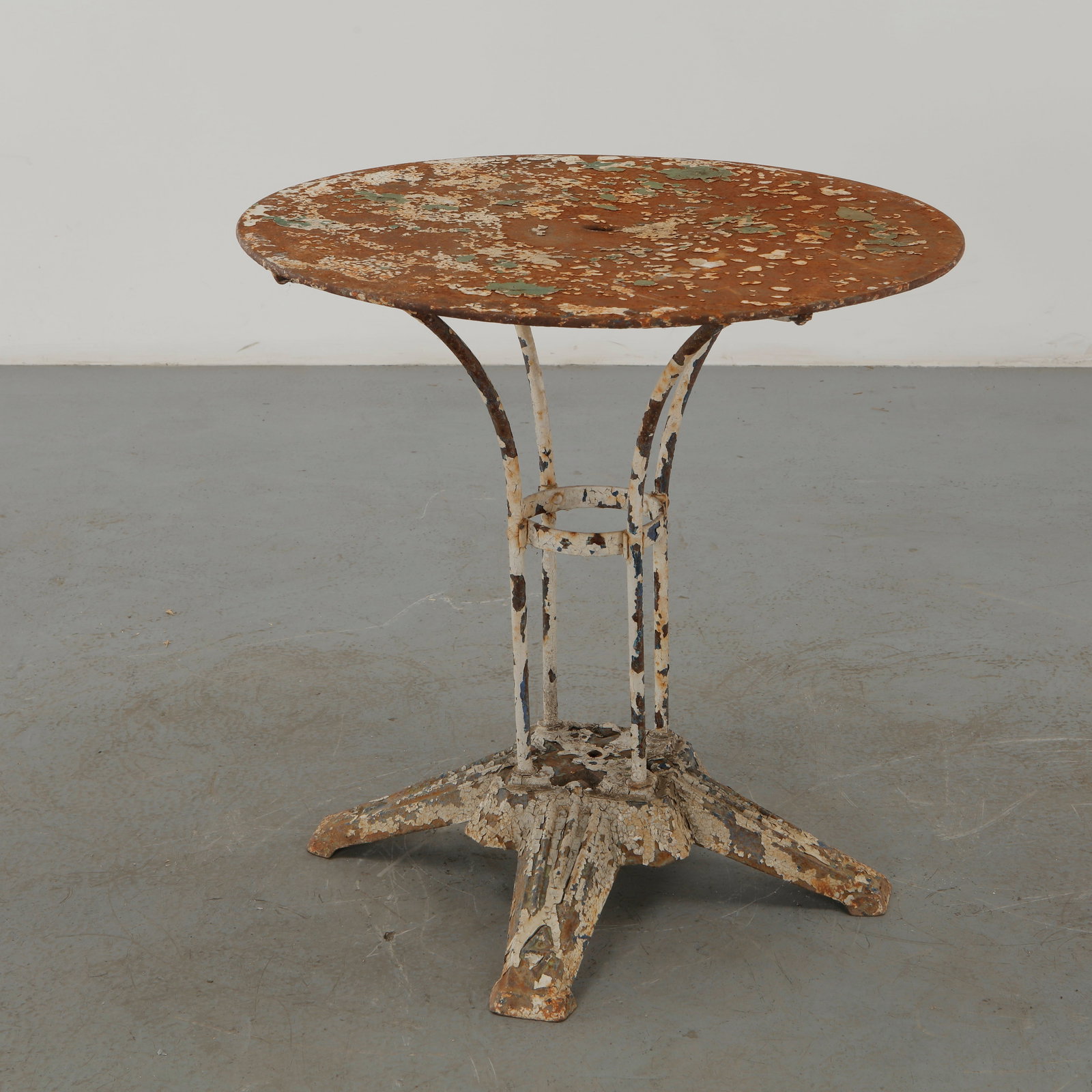 French Modernist Round Garden Table, 1960s: French modernist garden table featuring a circular metal top supported by an architectural wrought-iron base with radiating feet. The heavily weathered painted surface preserves a compelling layered