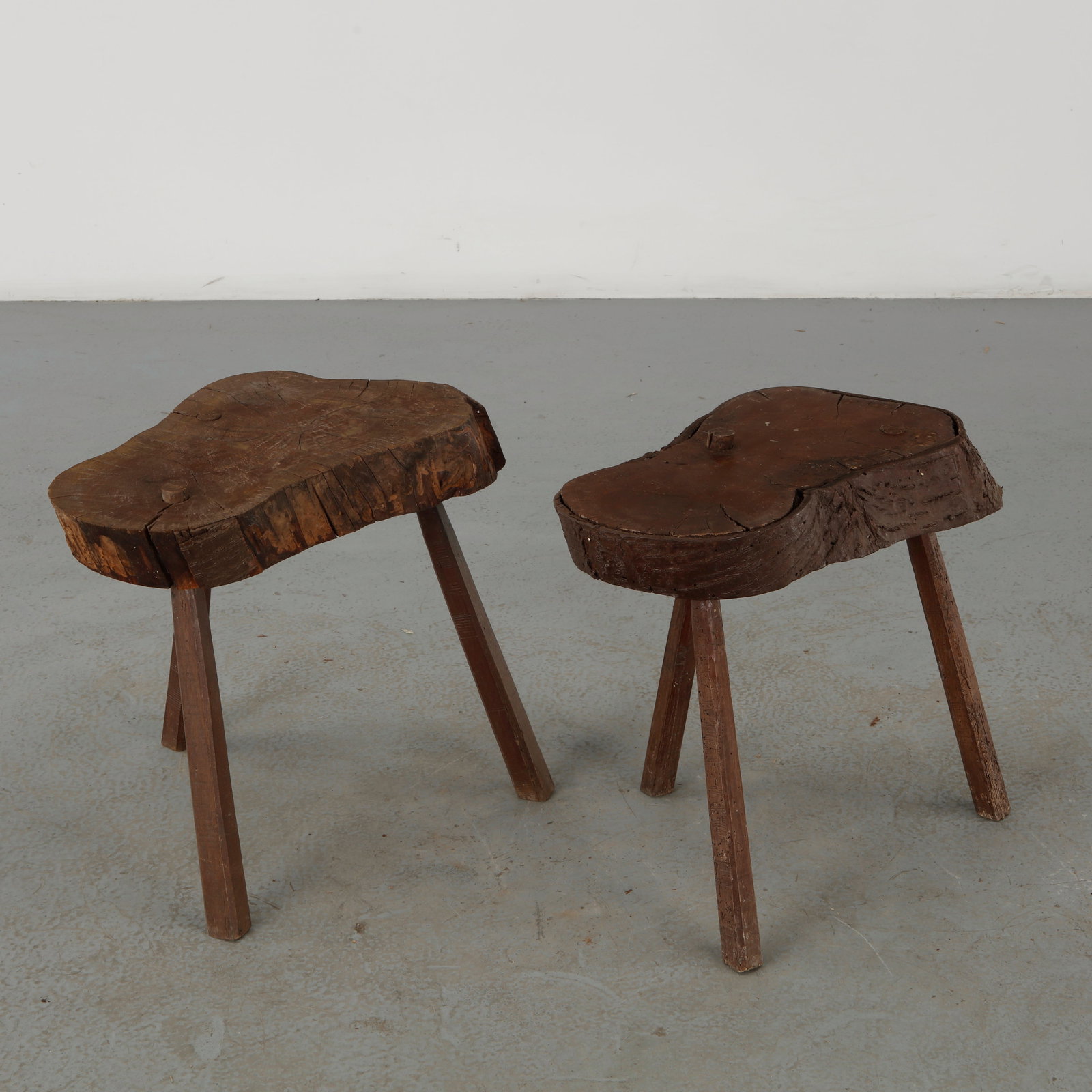 Pair of Brutalist Live Edge Wood Stools, 1960s: A pair of sculptural stools fashioned from irregular live-edge timber slabs, each retaining the natural contours, fissures and markings of the original wood. Their primitive construction and emphatic 