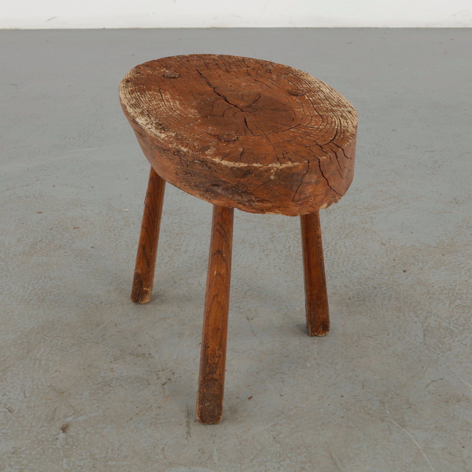 French Primitive Wooden Stool, 1960s: A rustic primitive stool crafted from a substantial section of solid wood, retaining the natural contours, growth rings, fissures, and irregularities of the timber. The simple three-legged constructio