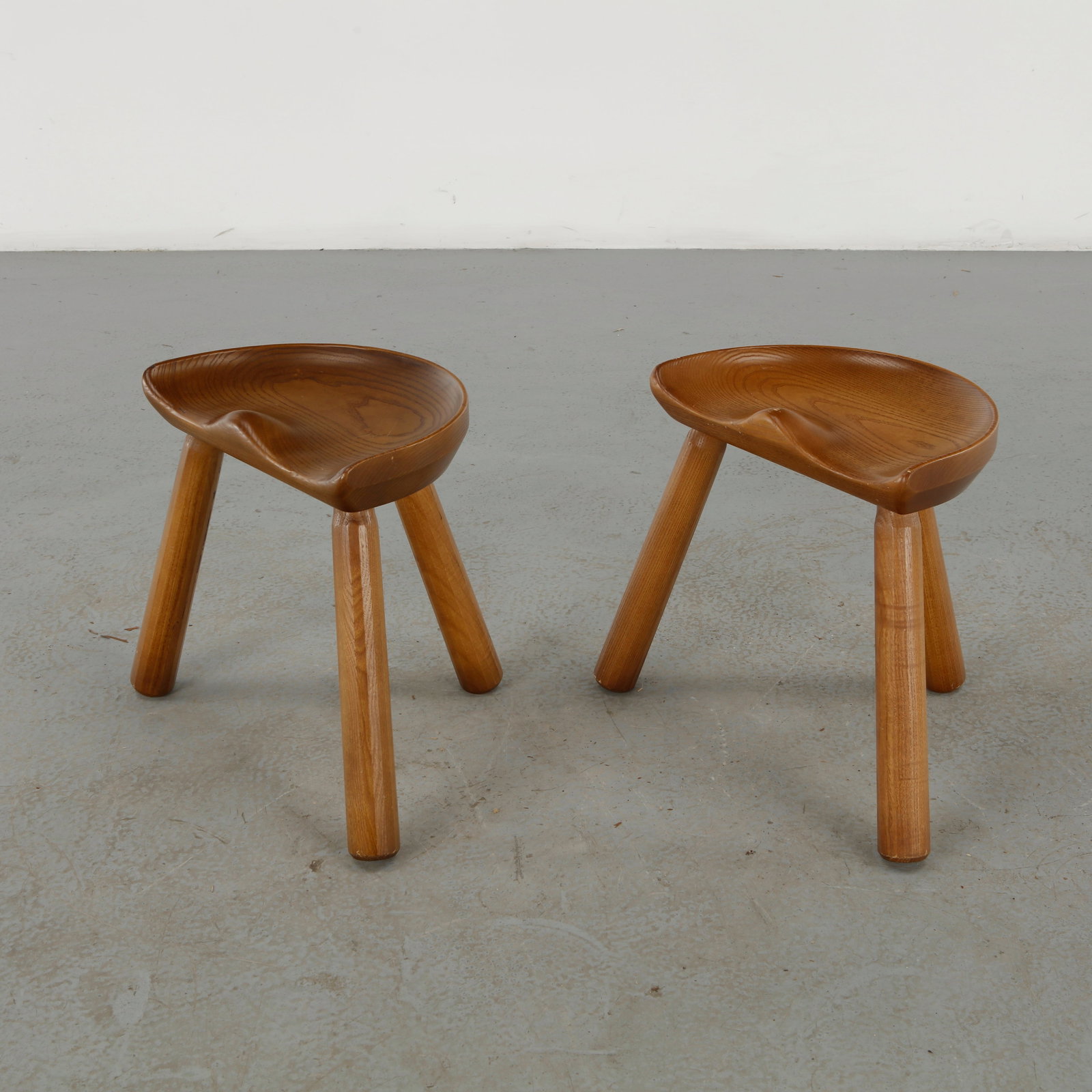Le Selou, Pair of Stools, 1960s: A refined pair of sculptural stools by Le Selou, featuring beautifully carved solid-wood seats with softly modeled, saddle-like contours and tapered legs. The exceptional grain and warm honey-toned fi