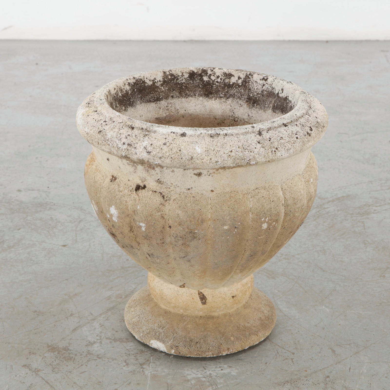 Cast Stone Urn Planter, 1960s: Cast stone urn planter with a fluted body, rounded rim, and classical pedestal base. The extensively weathered surface enhances its tactile quality and mature garden character. Height: 16 in.