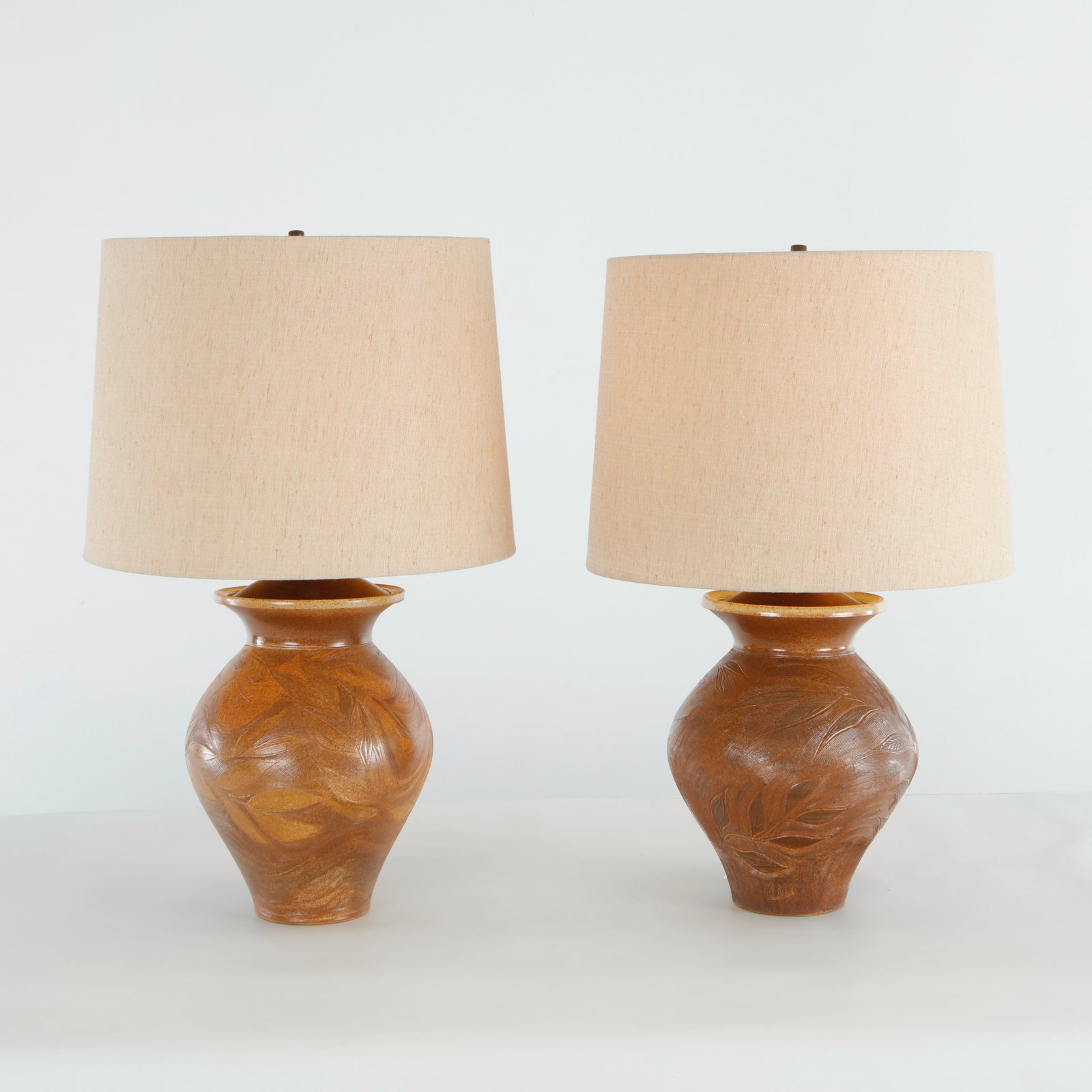Pair of Mid-Century Ceramic Table Lamps, 1960s: Pair of sculptural ceramic lamps featuring richly textured surfaces and warm organic forms. A refined expression of mid-century craftsmanship and decorative design. Working. Height: 27 in. Shade Diame