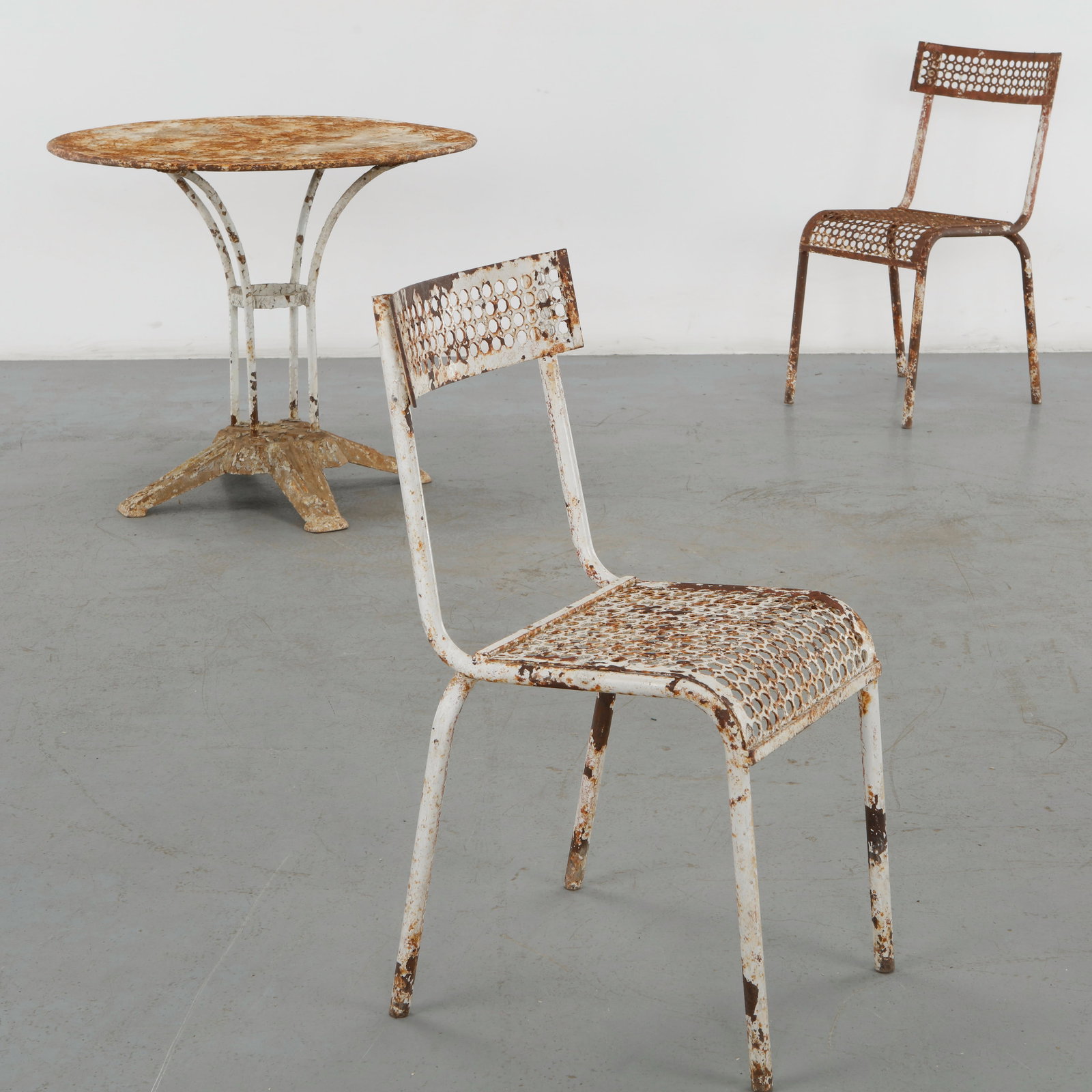 Parisian Outdoor Dining Set with Two Renee Malaval Chairs, 1960s: Outdoor dining ensemble comprising a round metal table and two perforated steel chairs, distinguished by slender curved supports and a weathered painted finish. The restrained construction and