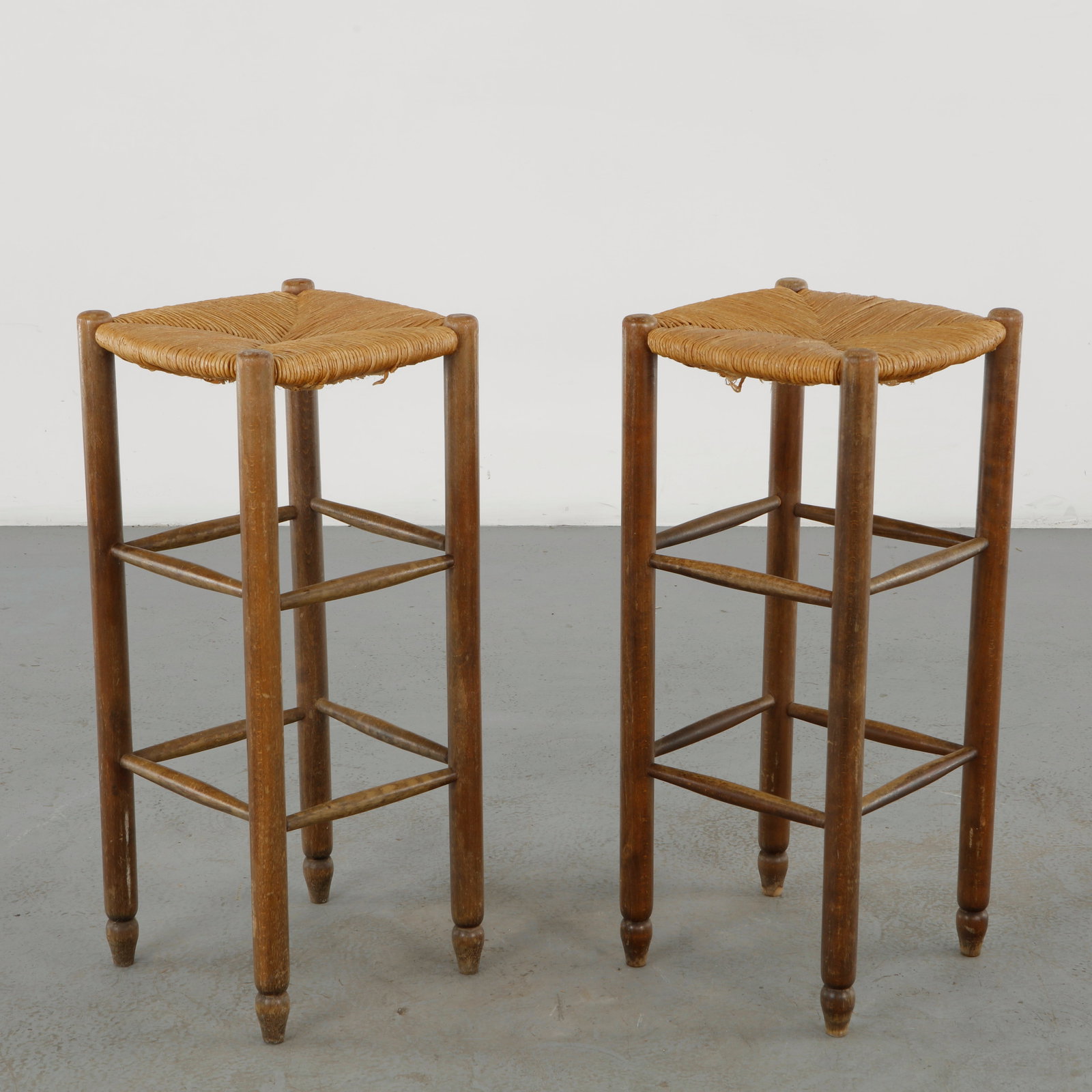 Pair of Rope Bar Stools, France, 1960s: A pair of rustic bar stools combining turned wooden frames with hand-woven natural-fiber seats. The tall proportions, articulated stretchers, and tactile woven surfaces demonstrate a refined