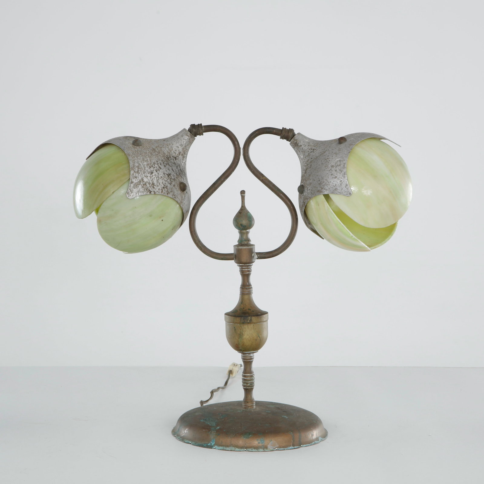 Double Lantern Tulip Table Lamp with Slag Glass Shades, 1930s: USA, early 20th century. Brass double-arm lamp in an S-scroll form, each arm terminating in a tulip-shaped shade of striated caramel-green slag glass, capped with pewtered metal petals. Raised on a tu