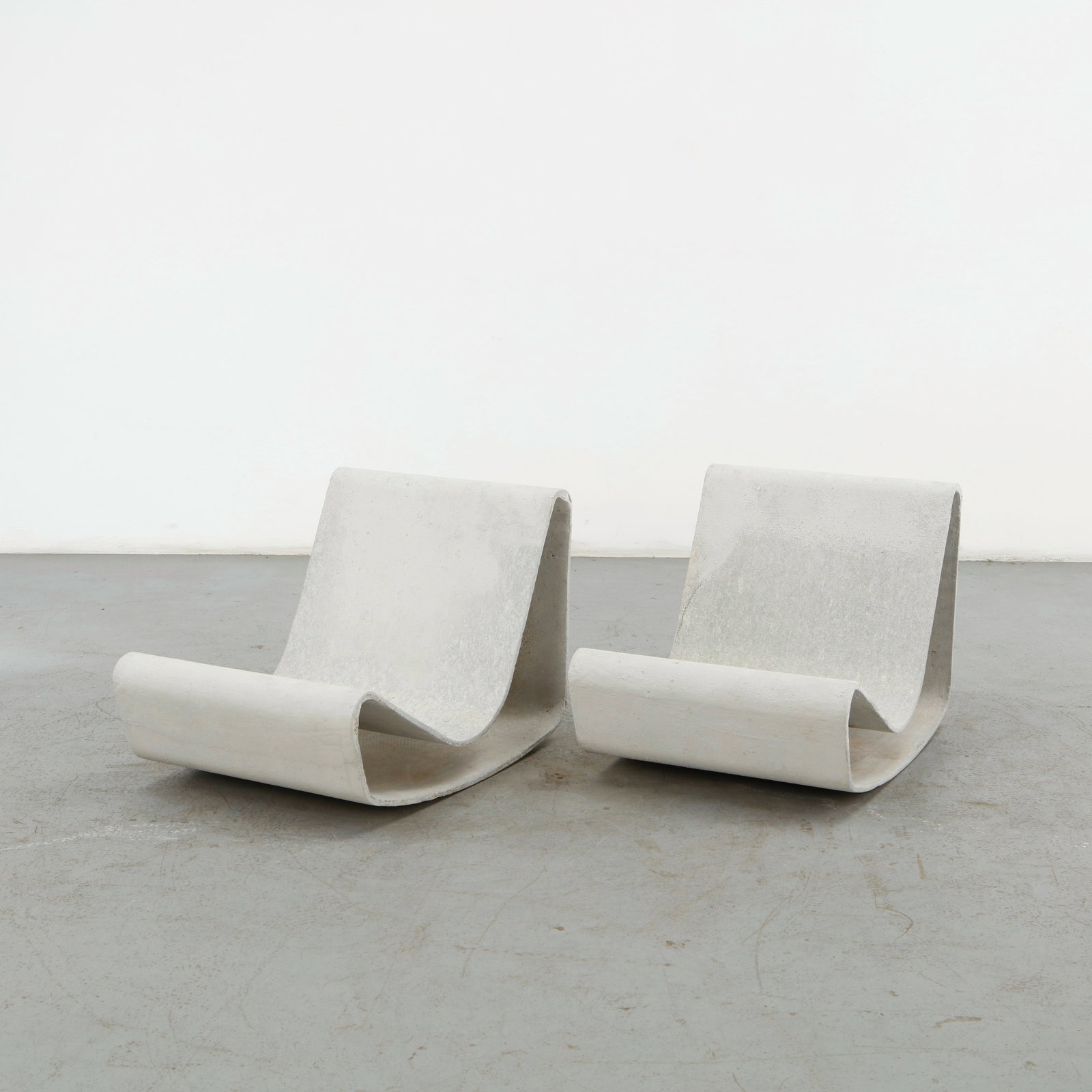 Willy Guhl, Pair of Loop Chairs, 1960s: A striking pair of sculptural lounge chairs crafted from fiber concrete with a weathered patina. The minimalist, curved design enhances their brutalist aesthetic, making them ideal for indoor or outdo