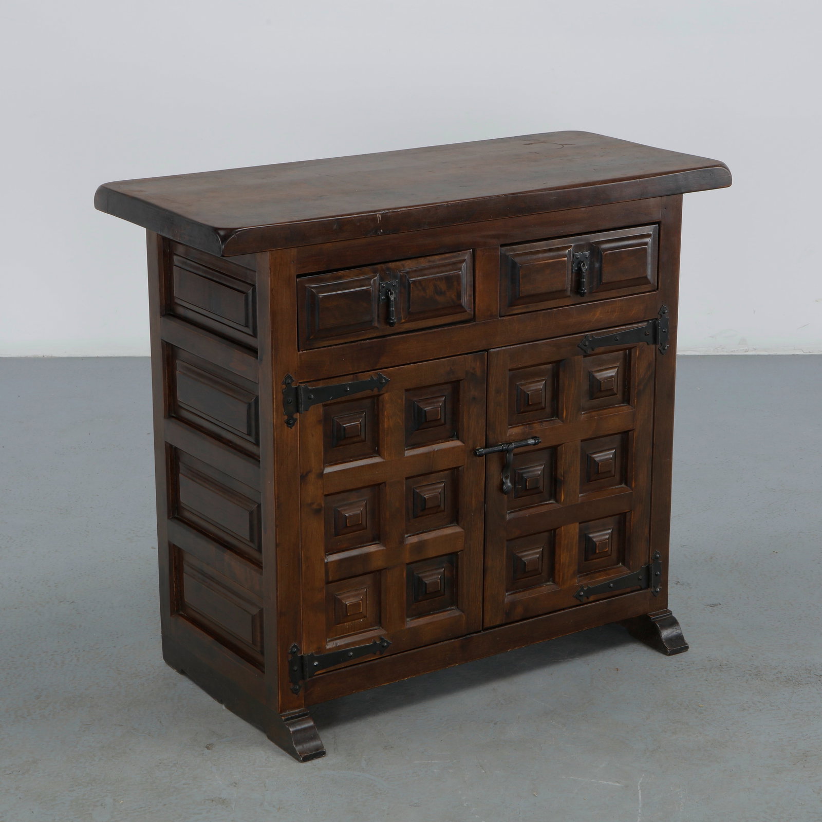 Spanish Carved Solid Wood Cabinet, 1960s: A Spanish cabinet in dark solid wood, its two doors and two drawers carved with a grid of raised square panels, fitted with black wrought iron strap hinges and a forged latch, standing on curved brack