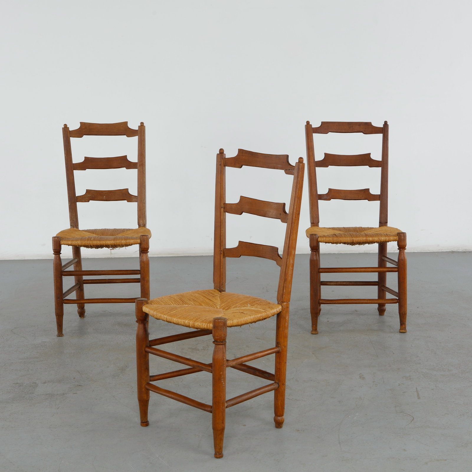 Set of Three Rustic Ladder-Back Chairs, 1960s: This set of three rustic ladder-back dining chairs represents a timeless French Provincial or country-style design. These chairs beautifully capture a traditional folk aesthetic, balancing robust, han