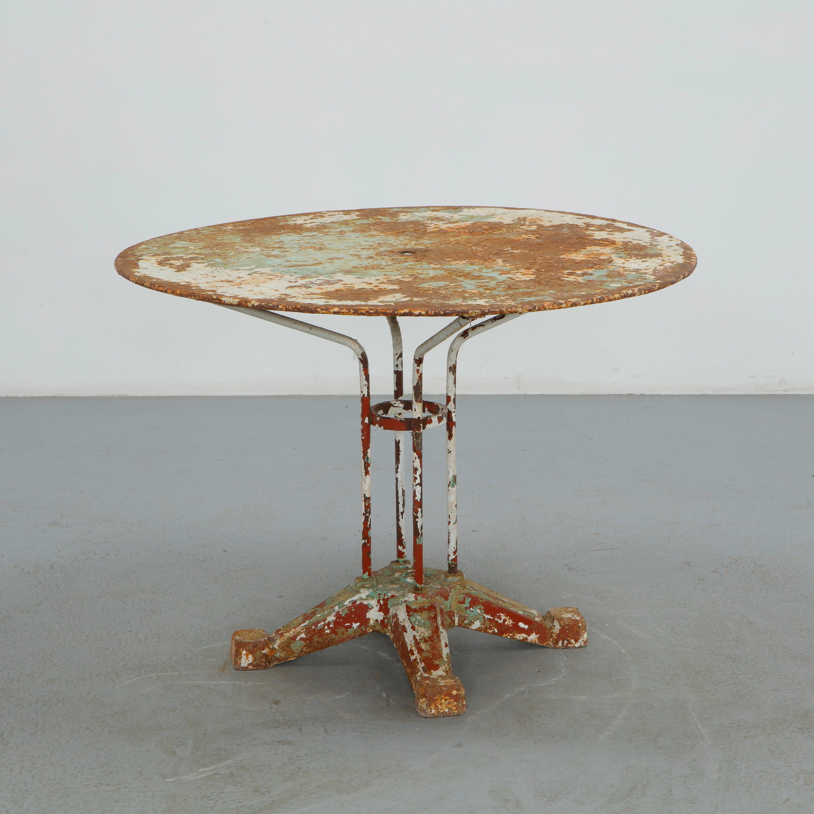 Round Parisian Metal Garden Table, 1950s: Constructed from painted metal, this round garden table is raised on a four legged base with a central umbrella ring. The heavily weathered surface, with losses revealing layers of red, green, and whi