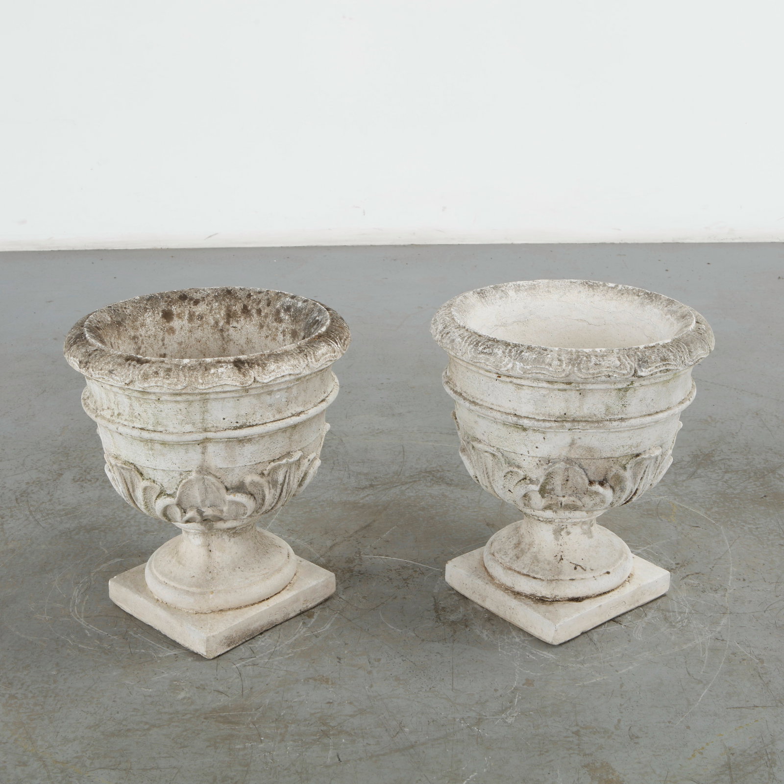 Pair of Stone Urn Planters, 1960s: This pair of cast stone urn planters showcases a beautiful Neoclassical style, highly valued for mid-century garden ornamentation. It is intricately molded with a bold relief pattern of acanthus leave