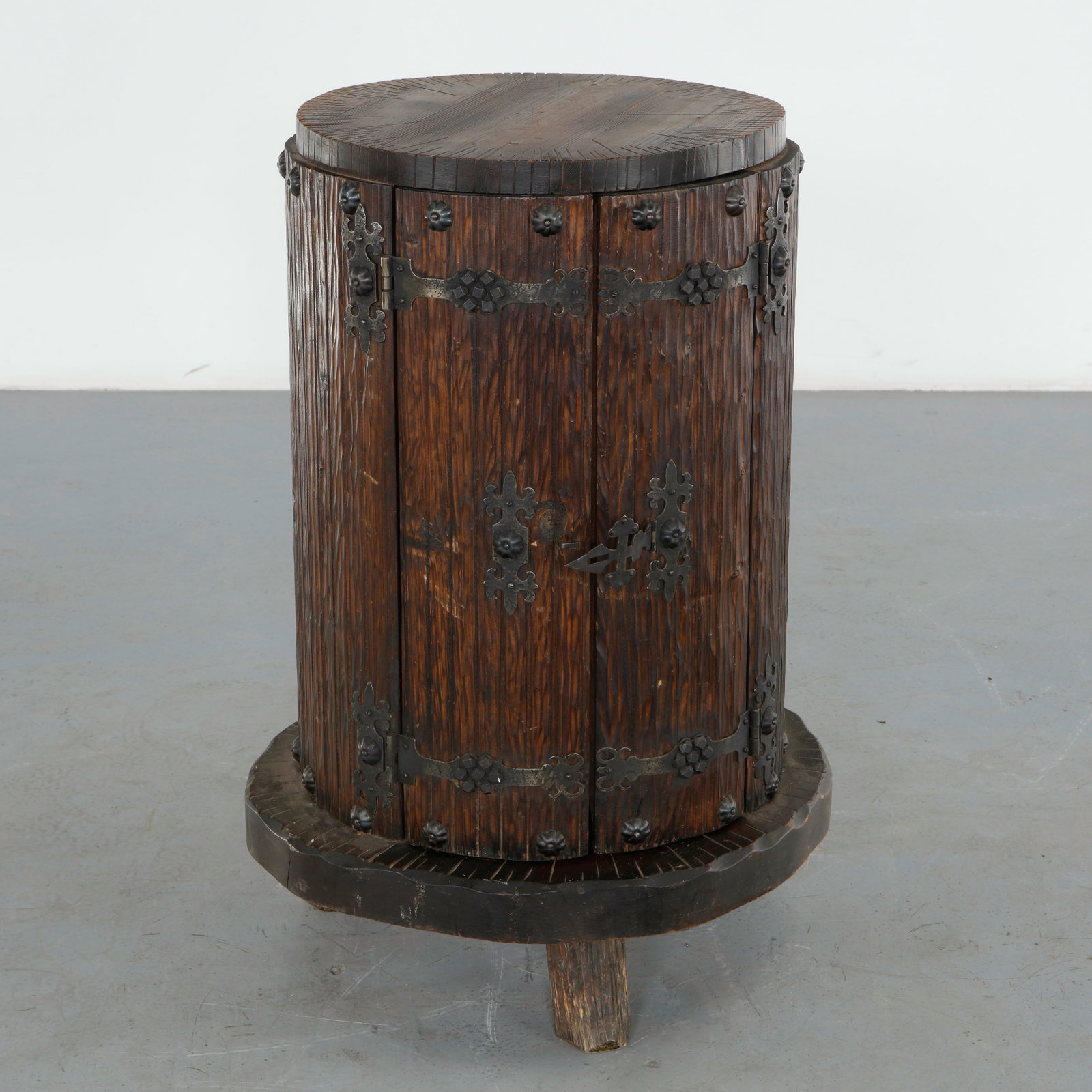 Brutalist Cylindrical Cabinet, 1960s: Constructed from solid wood, this cylindrical cabinet features two curved doors bound in hand wrought iron straps and rosette studded hardware, raised on a tripod sculptural log form legs. The dense, 
