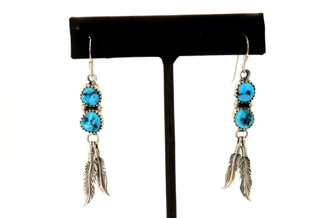 2 Stone AAAA Sleeping Beauty Turquoise Earrings: Navajo 2-stone AAAA sleeping beauty turquoise with gold matrix. Earrings stones are 1/4" diameter bezel-set sterling silver with (2) sterling silver hand-tooled feathers L 2 3/4"x 3/8"W. One of a kind