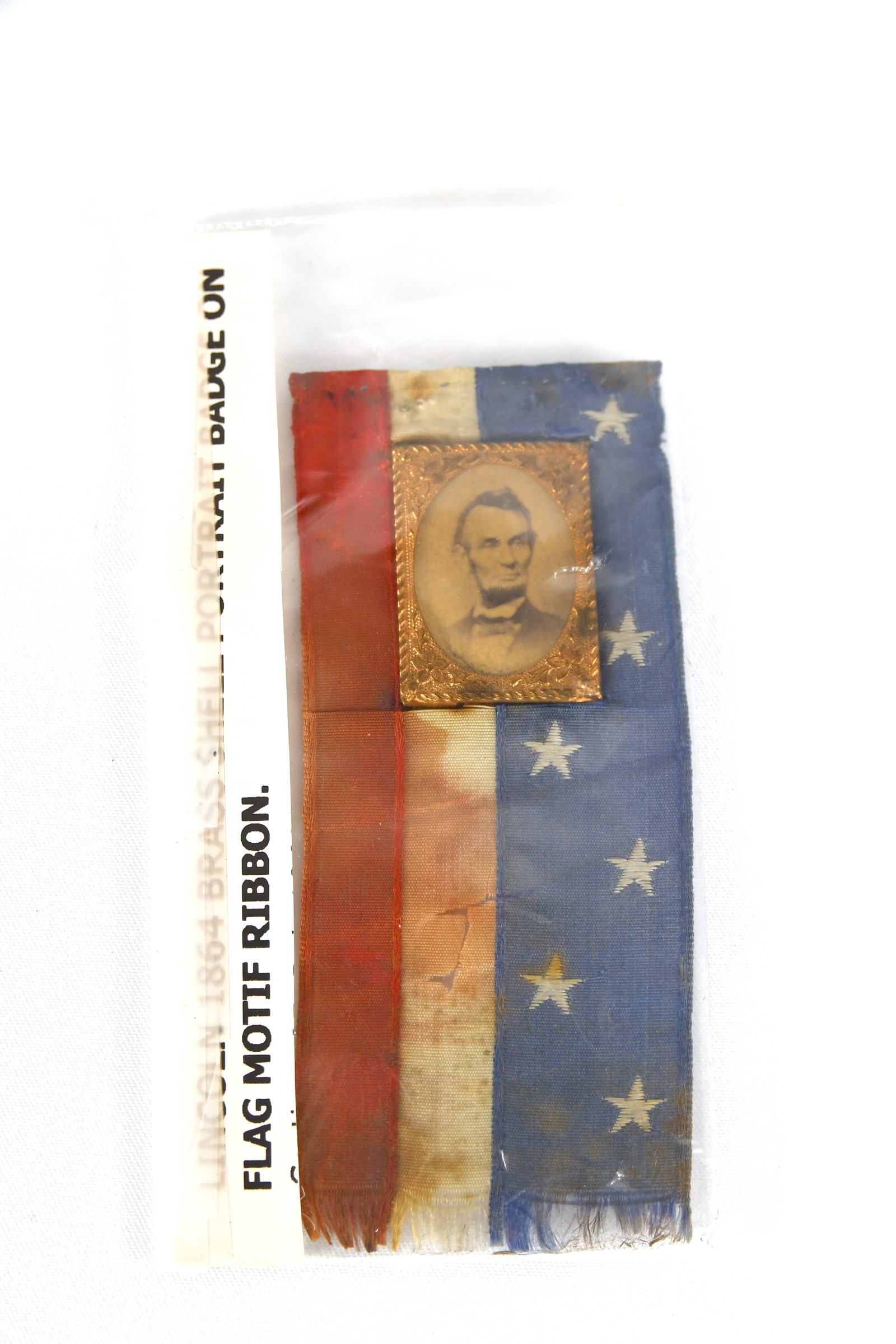 Abraham Lincoln 1864 Gem Albumen Campaign Ribbon: Abraham Lincoln 1864 Gem Albumen Campaign Ribbon Abraham Lincoln 1864 brass shell portrait badge on American flag motif ribbon The tag on back of the ribbon reads "Made by S.A. Blake, 407 Broadway, NY