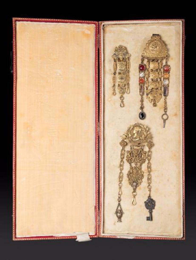 Trois châtelaines en métal doré et argenté et pierres: Trois châtelaines en métal doré et argenté et pierres dures ; dans un écrin en maroquin rouge doré aux petits fers. L (écrin) : 44 cm. Three gilt-metal châtelaines, H.:17.3/8 in