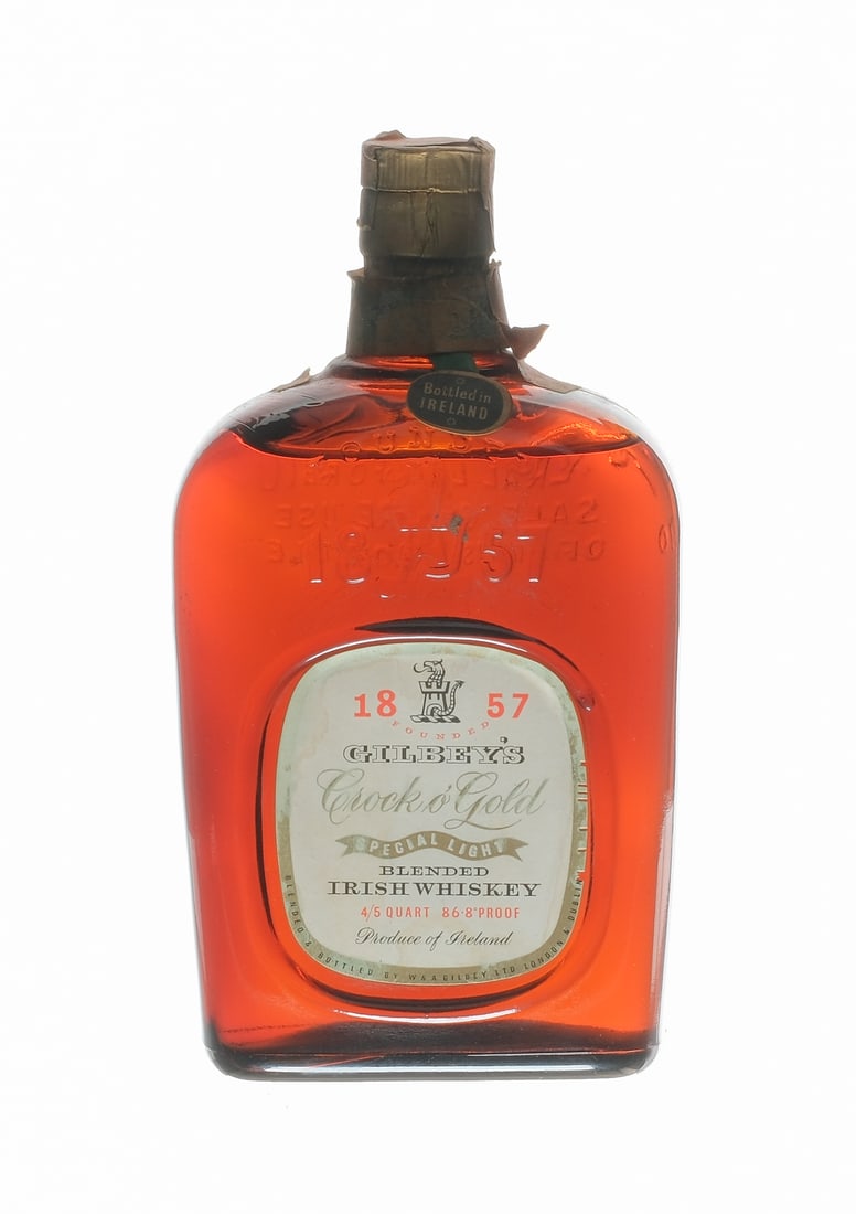 Gilbey's Crock o'Gold Spec. Light Whiskey Blend: Description 86.8 Proof. Foil intact. Bottle stamp broken. Paper wraparound is loose. "Bottled in Ireland" hang tag intact (though ribbon is frayed at one end). Labels exhibit wear, staining and small 