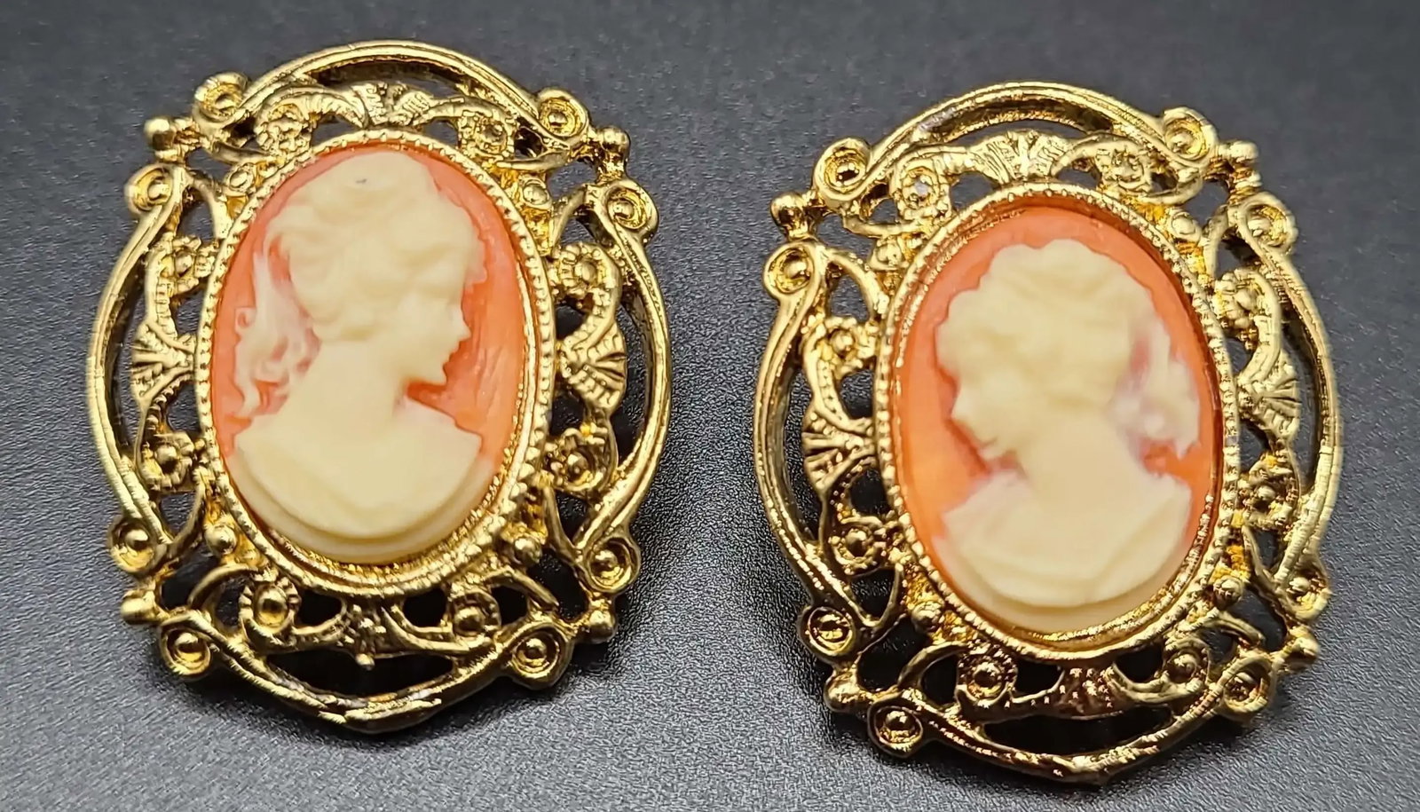 Vintage Gold Tone Cameo Earrings - Lady Portrait Filigree: Lovely pair of vintage cameo earrings featuring classic lady profile carvings in soft cream tones set against a warm coral background. Each cameo is framed by an ornate gold-tone filigree setting with