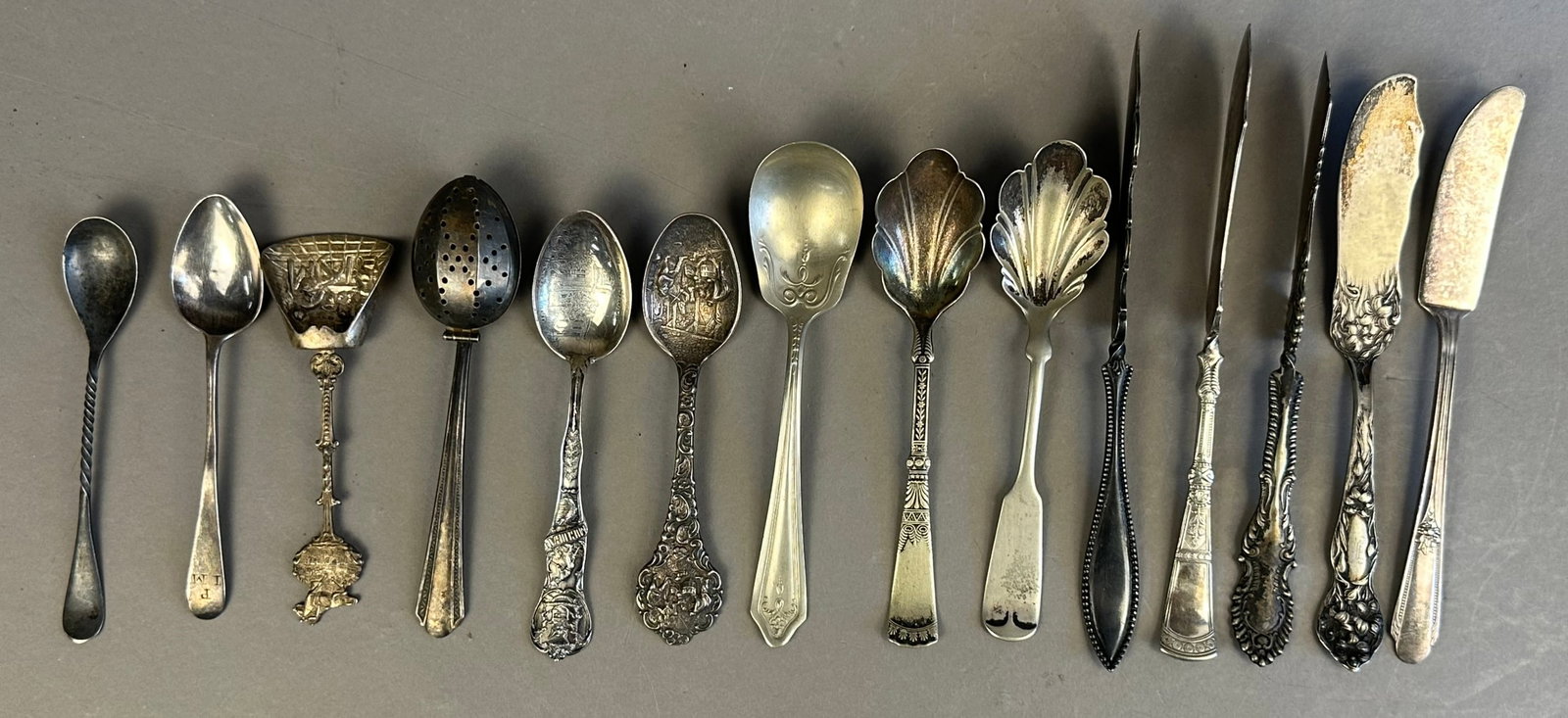 14 Ornate Spoon Knife Silver Plate & Sterling Lot: This lot includes 5 ornate Stratford, Rogers butter knives. 7 spoons and tea strainer. 1 marked sterling weighing 20 grams, marked Hanover Michigan.