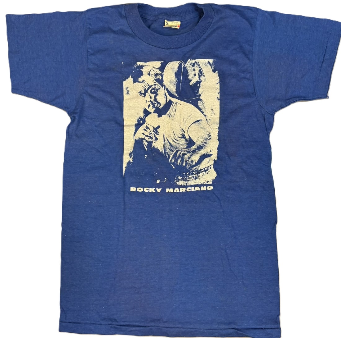 Rocky Marciano Original 1970s Screen Stars Boxing T-Shirt Size Small: Incredible original Rocky Marciano t-shirt by Screen Stars. Size small. PLEASE NOTE WE OFFER IN HOUSE SHIPPING & HAVE BIDDING AVAILABLE ON OUR OWN WEBSITE! If you win on LIVE AUCTIONEERS, please click