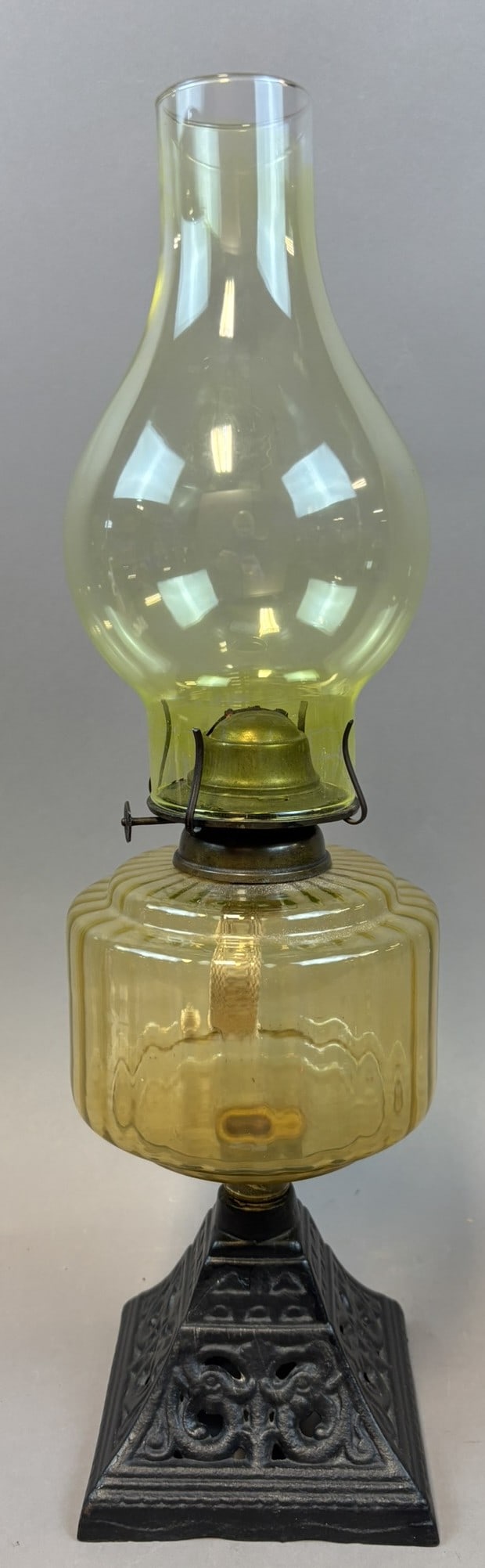 Uranium Vaseline Glass Oil Lamp w/ Cast Iron Ornate Base 19.5": Late 19th to early 20th century kerosene oil lamp featuring a ribbed uranium (vaseline) glass font with matching yellow-green glass chimney mounted on an ornate cast iron base with pierced decorative