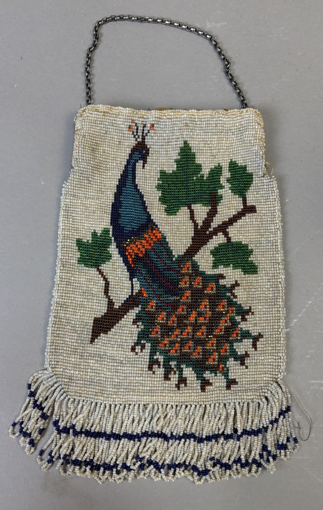 Antique Beaded Peacock Purse w Fringe & Chain Handle 11x7: A charming antique hand-beaded purse featuring a beautifully detailed peacock perched upon a leafy branch. Executed in fine glass seed beads, the design showcases rich blues, greens, and warm orange t