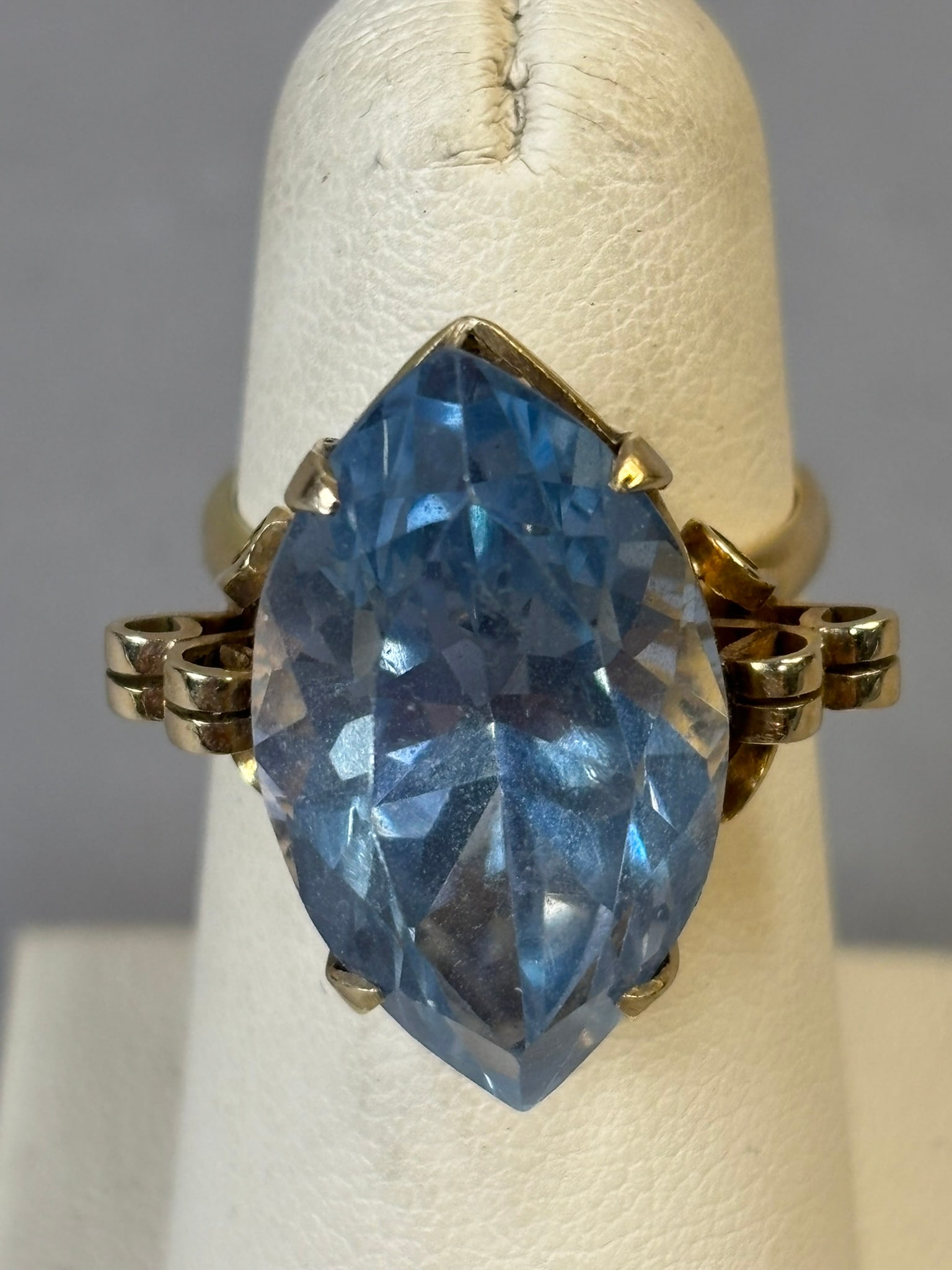 14K Gold Large Marquise Blue Glass Stone Ring 9.4 Grams Estate Statement: Offered here is a striking 14K yellow gold estate ring set with a impressive marquise-cut blue glass. The glass displays a vibrant, deep blue hue with lively faceting that captures and reflects light