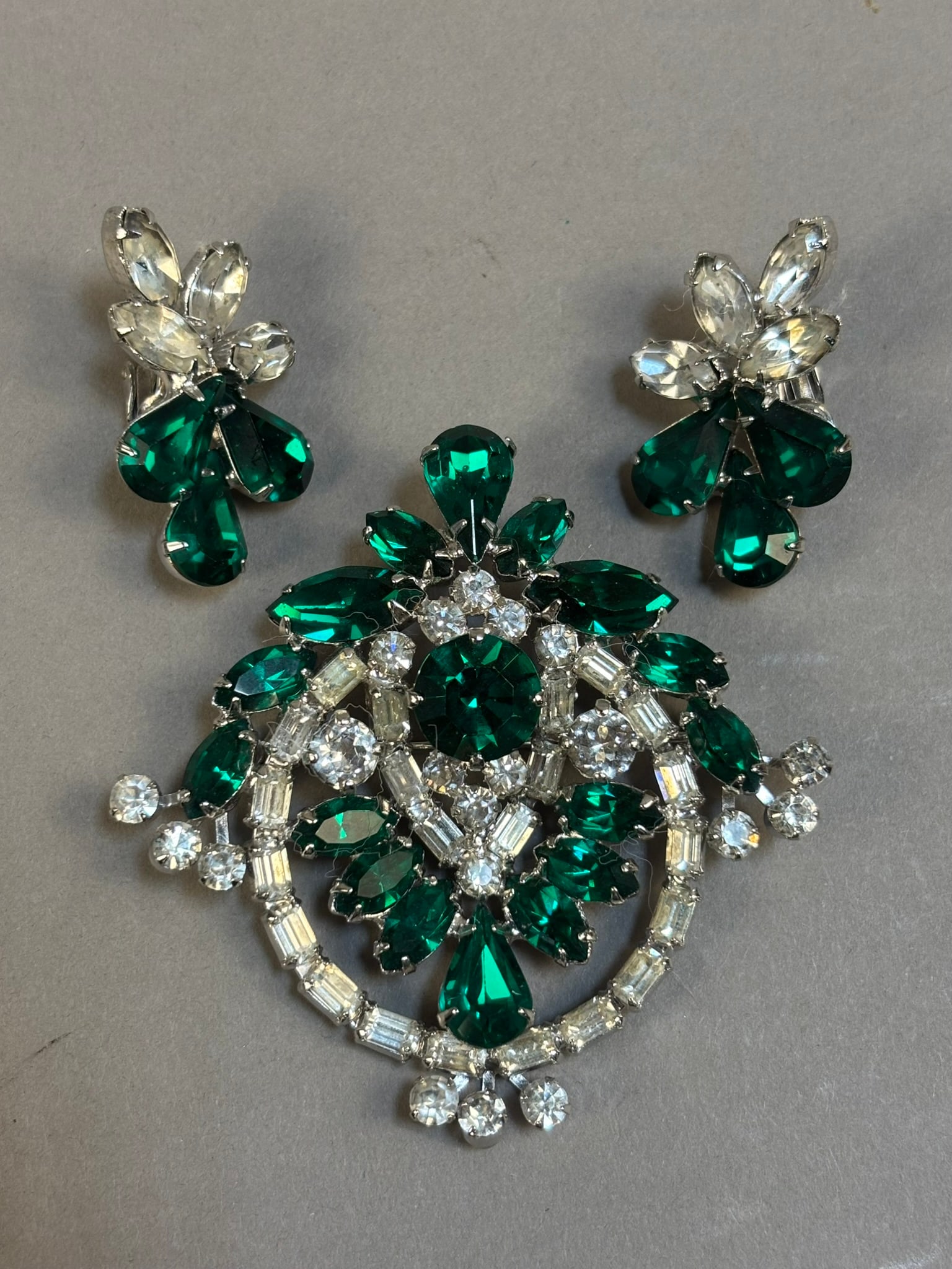 Vintage Emerald Green Rhinestone Brooch w Matching Clip Earrings Set: Striking vintage rhinestone brooch and matching clip-on earrings set featuring vibrant emerald green teardrop and marquise cut stones accented by clear round and baguette rhinestones in an ornate circ
