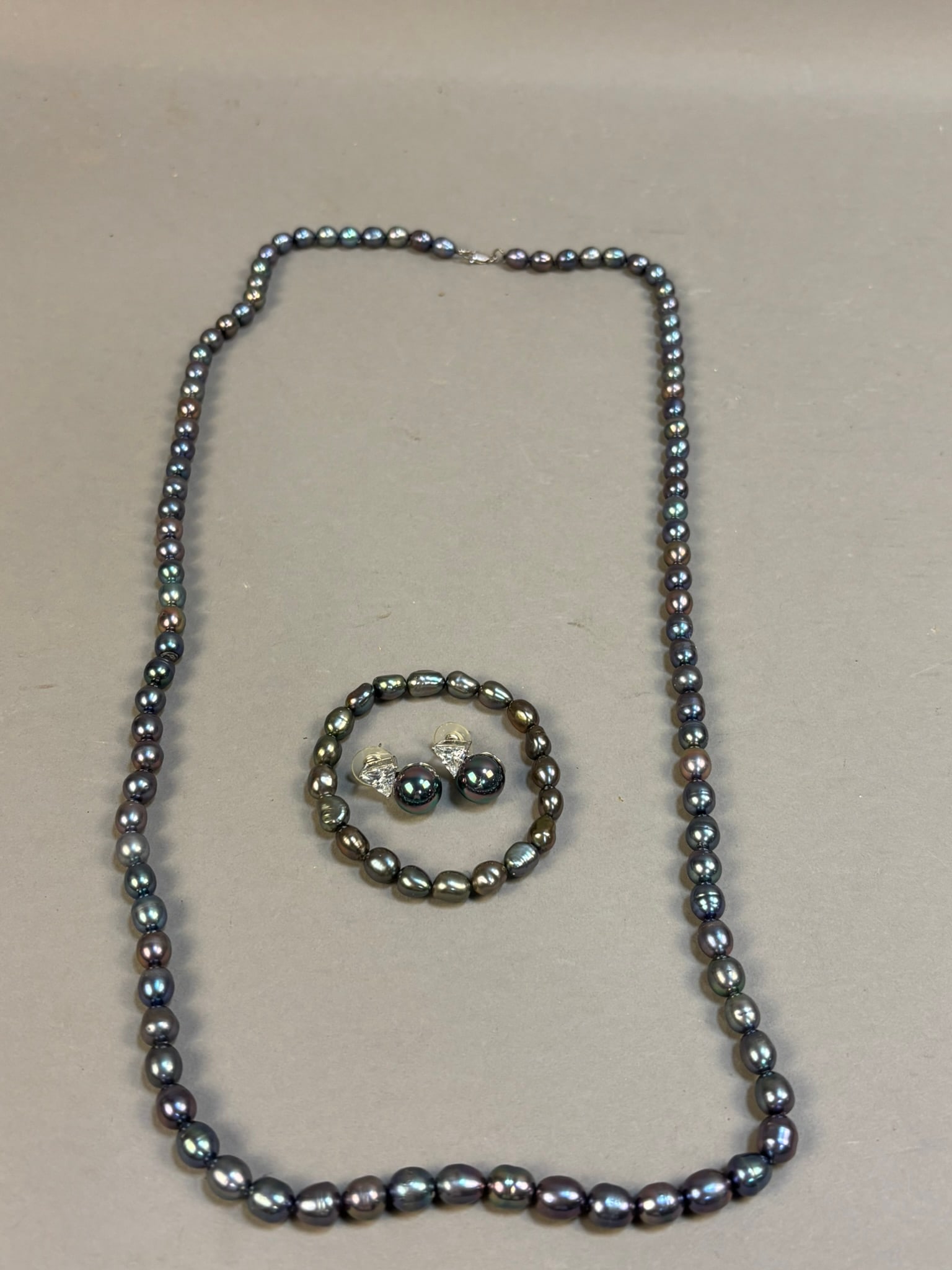 Black Freshwater Pearl Necklace Bracelet 925 Earrings Set Peacock Luster: Elegant black freshwater pearl jewelry set including a strand necklace, matching stretch bracelet, and a pair of stud earrings set with peacock-luster pearls and triangular cubic zirconia accents. The