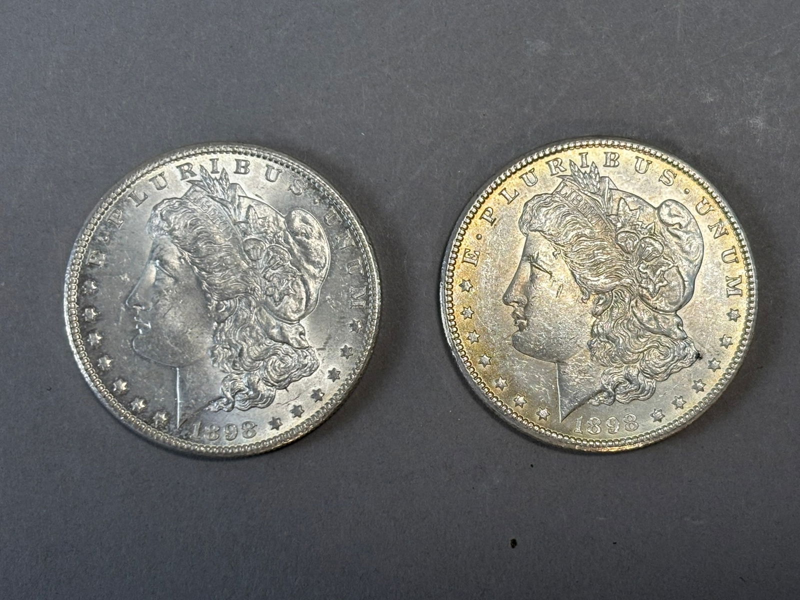 1898 Morgan Silver Dollars Pair 53.4g Combined US $1 Coins: Pair of 1898 United States Morgan silver dollars, each struck in 90% silver and featuring the classic Liberty head obverse and eagle reverse designed by George T. Morgan. Both coins show circulated