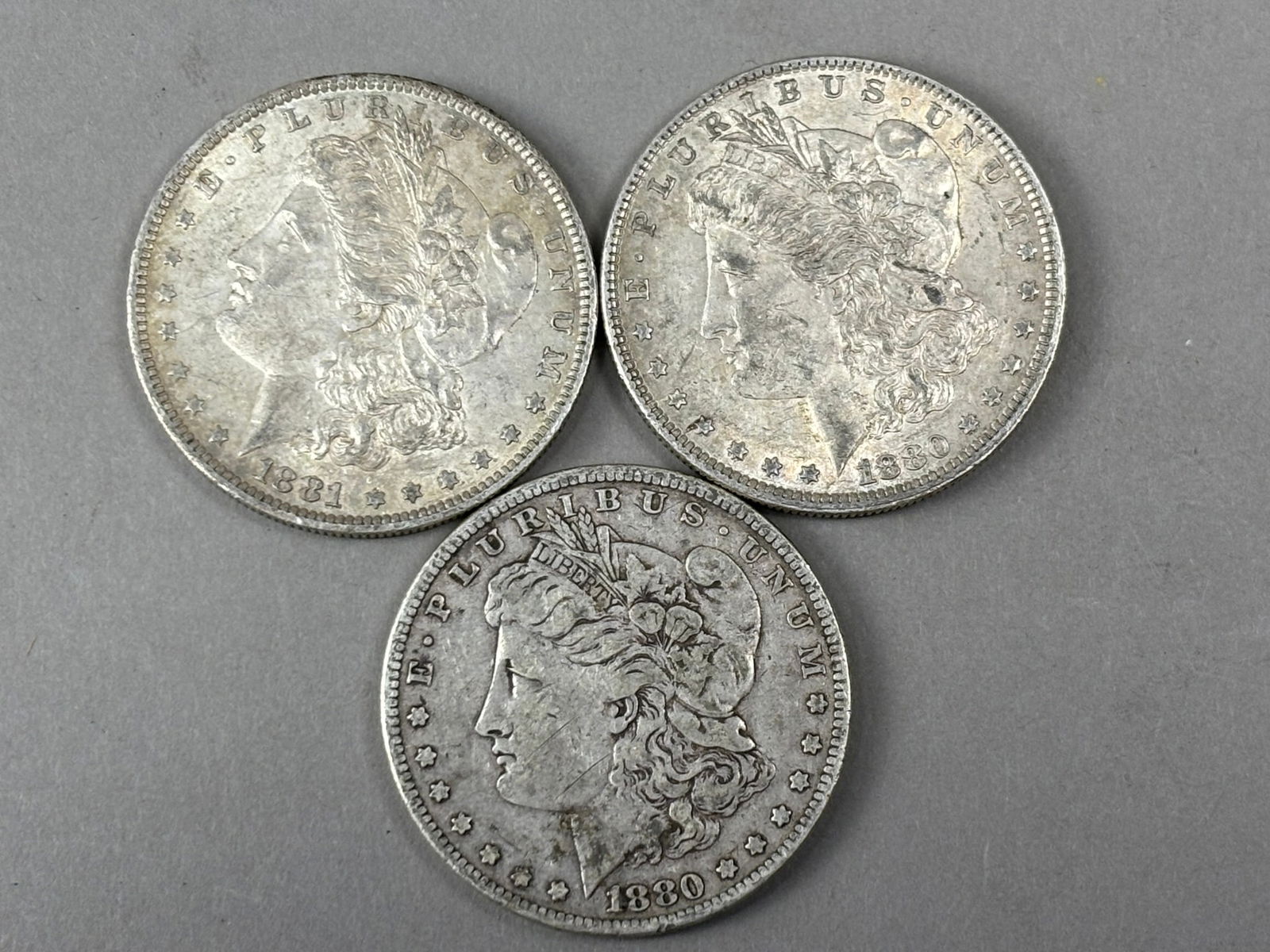 Group of Three Morgan Silver Dollars 1880 & 1881 Mixed Circulated Coins: Group of three United States Morgan silver dollars including two dated 1881 and one dated 1880, each featuring the Liberty head obverse and eagle reverse designed by George T. Morgan. The coins show c