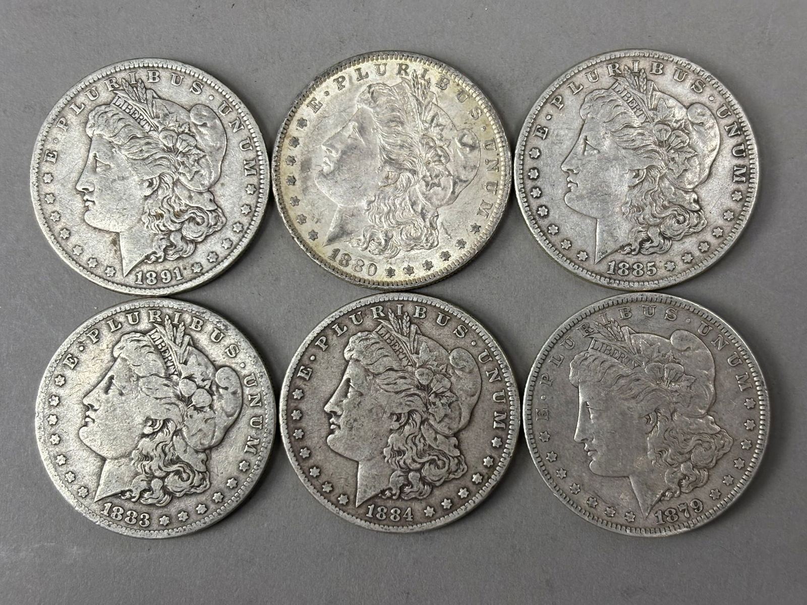 Six Morgan Silver Dollars 1879–1891 Mixed Dates Circulated Coins: Group of six United States Morgan silver dollars consisting of mixed dates including 1879, 1880, 1883, 1884, 1885, and 1891. Each coin displays the classic Liberty head design by George T. Morgan and