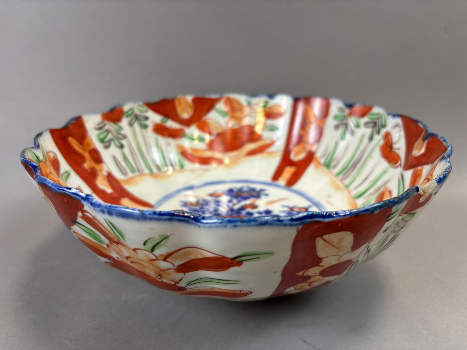 Japanese Imari Porcelain Scalloped Bowl Floral Basket Motif 9.75": Japanese Imari porcelain scalloped rim bowl featuring a traditional underglaze cobalt blue and iron-red palette with green enamel highlights. The interior centers a floral basket motif within a blue c