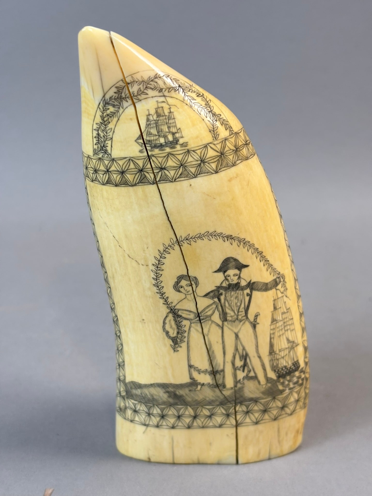19th C Scrimshaw Whale Tooth George Robinson Family Provenance: Important 19th century scrimshaw whale tooth engraved with a romantic maritime scene depicting a gentleman and lady standing beneath a wreath cartouche with a finely detailed sailing vessel beside the
