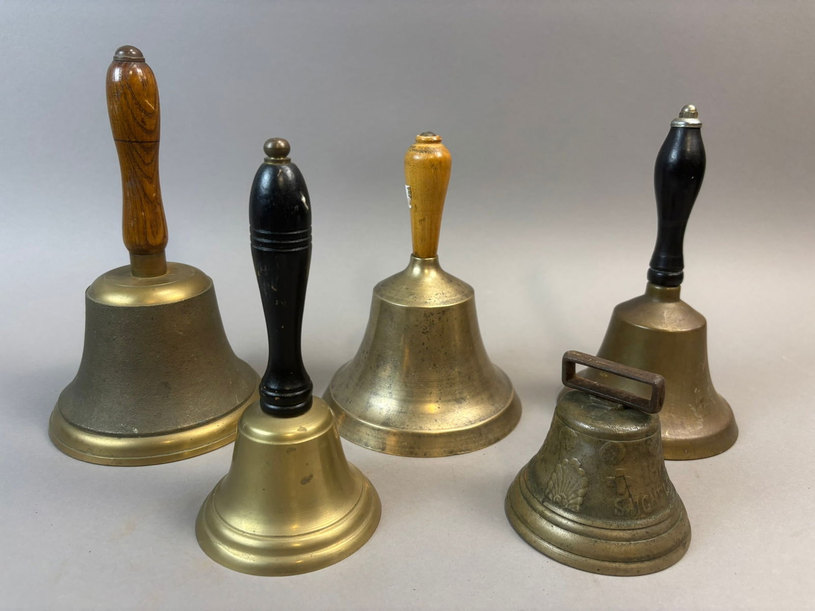 Antique Lot 5 Brass School Hand Bells Wood Handles Classroom Teacher Bells 1878: Collection of five vintage brass hand bells with turned wood handles including several classroom or teacher’s bells used historically in schools, shops, and service counters to signal attention.