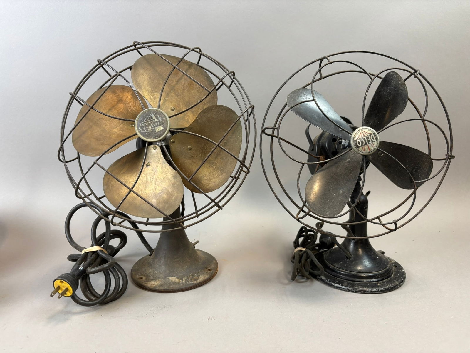 Emerson Electric Brass Blade Desk Fan & Delco Oscillating Desk Fan Pair: Pair of vintage electric desk fans including an Emerson Electric fan with four brass blades and wire cage and a Delco oscillating desk fan with four black metal blades and original badge. Both retain