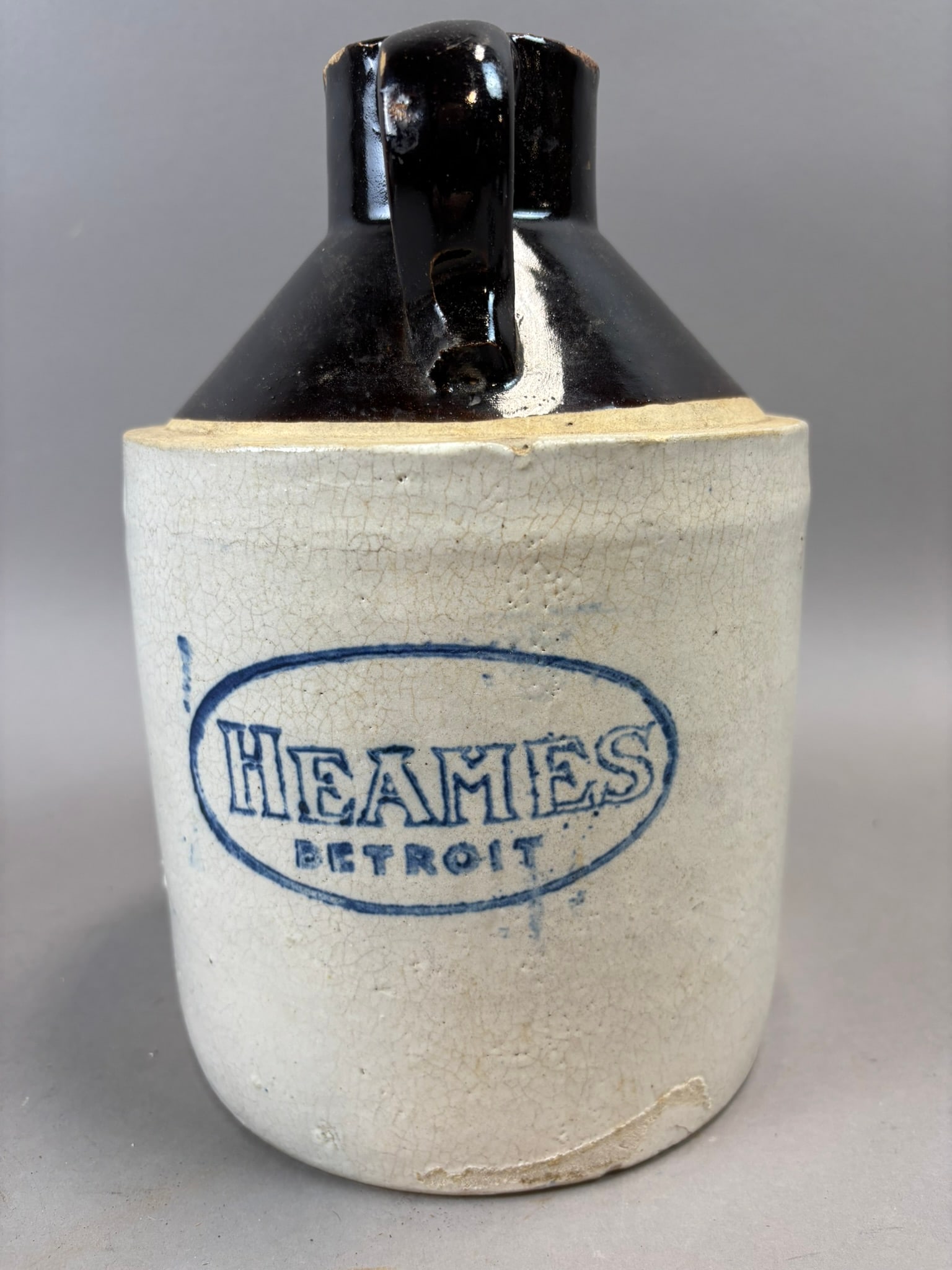Heames Detroit Stoneware Jug Albany Slip Top Advertising Crock: Antique advertising stoneware jug bearing the cobalt stamped oval mark “Heames Detroit,” featuring a classic two tone glaze with cream colored body and dark Albany slip glazed shoulder and