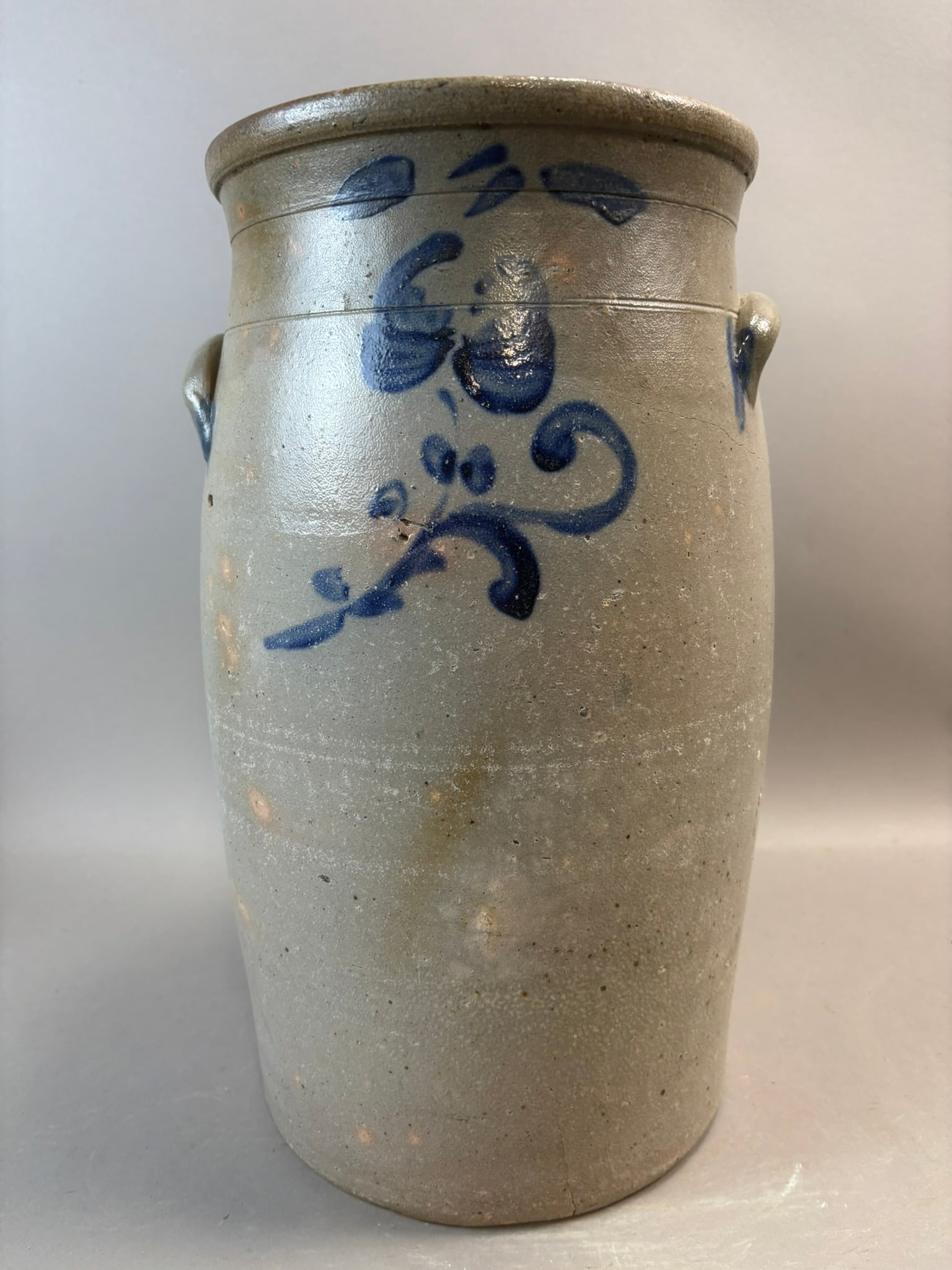Antique American Stoneware 6 Gallon Butter Churn Cobalt Floral Decoration: Antique American stoneware butter churn featuring hand-painted cobalt floral decoration on a tall cylindrical form with applied lug handles and rolled rim. The body displays a classic salt-glazed gray