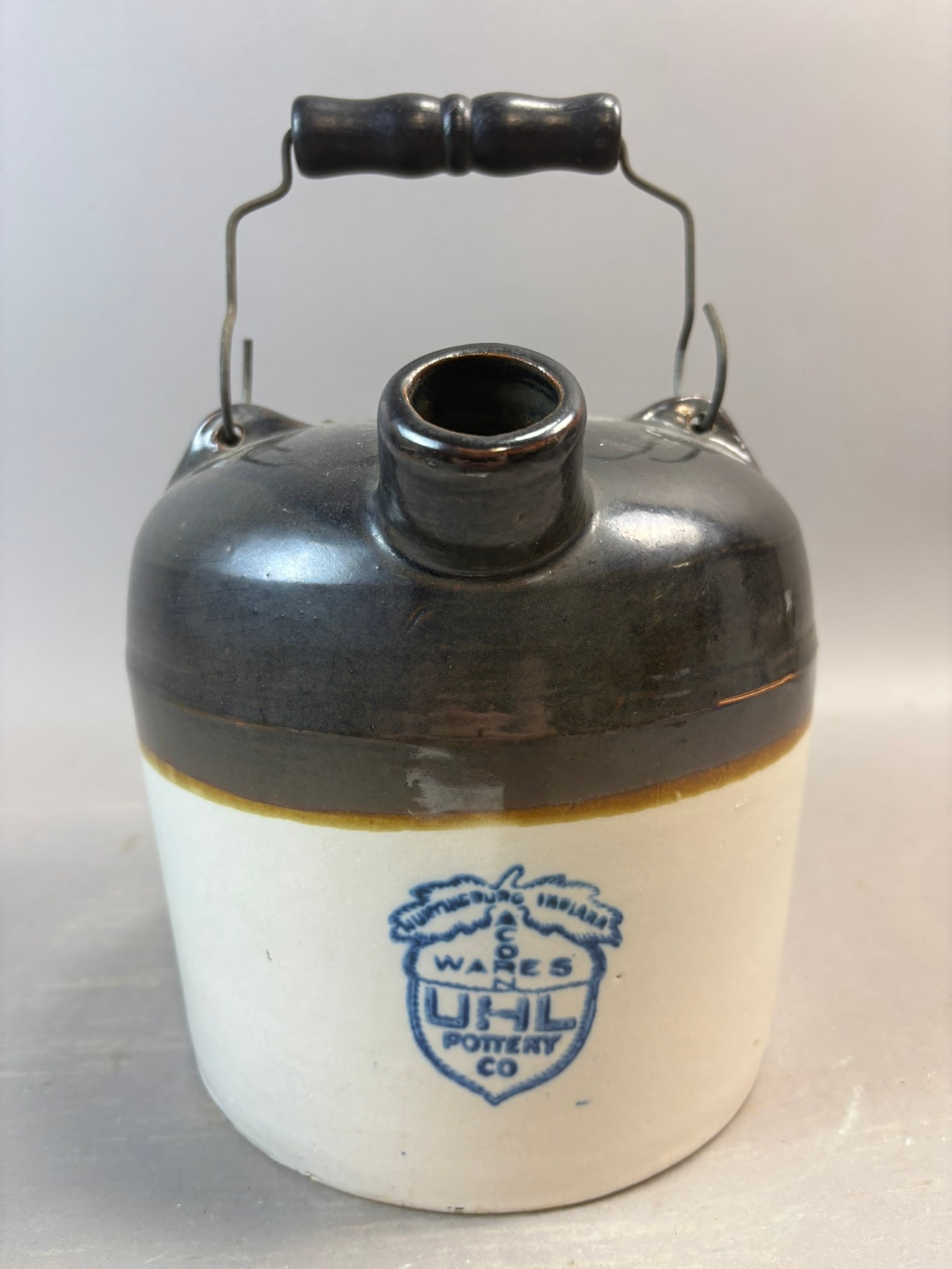 UHL Pottery Co Huntingburg Indiana Stoneware Whiskey Jug Brown Top: Two-tone American stoneware whiskey jug produced by UHL Pottery Company of Huntingburg, Indiana, featuring a classic cream glazed body with dark brown Albany slip glazed shoulder and spout. The jug re